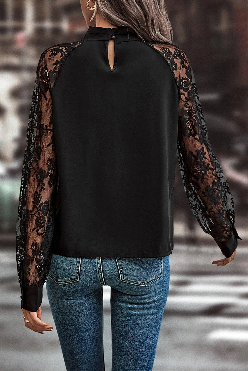 Black blouse with sheer lace sleeves worn by a person, blurred background