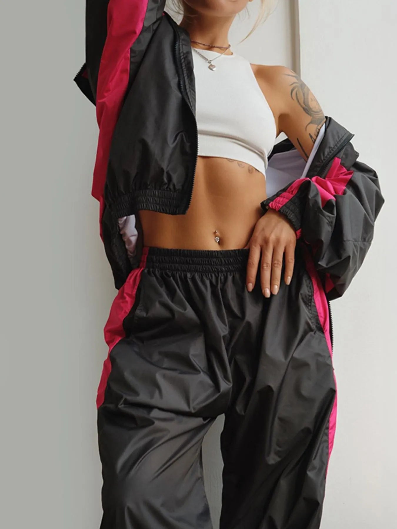 Person wearing a black and pink jacket with a white top and pants on a plain background