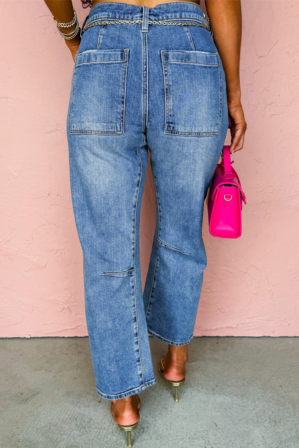 Person wearing blue jeans and holding a pink bag against a pink wall.