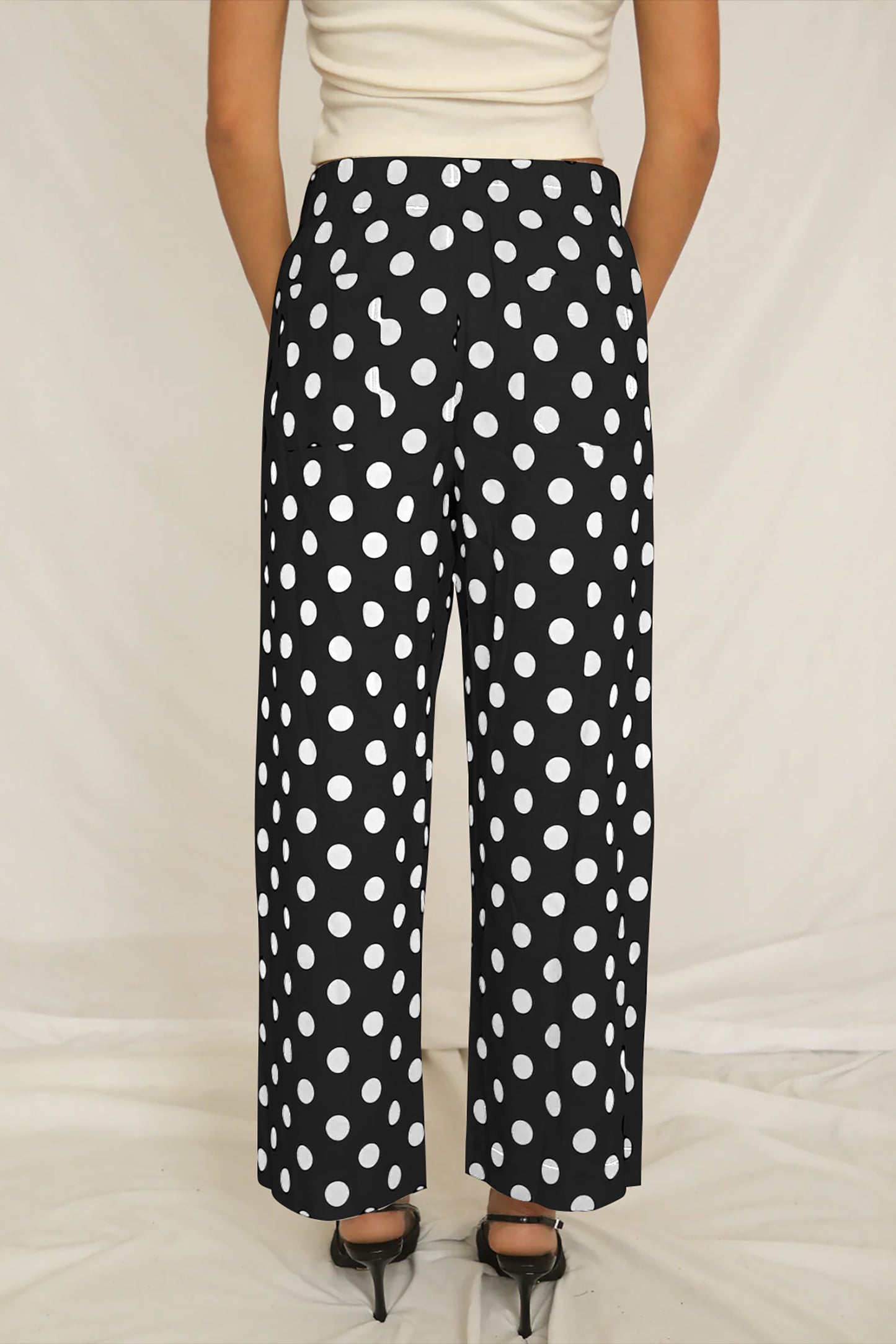Person wearing black pants with white polka dots on a plain background back view