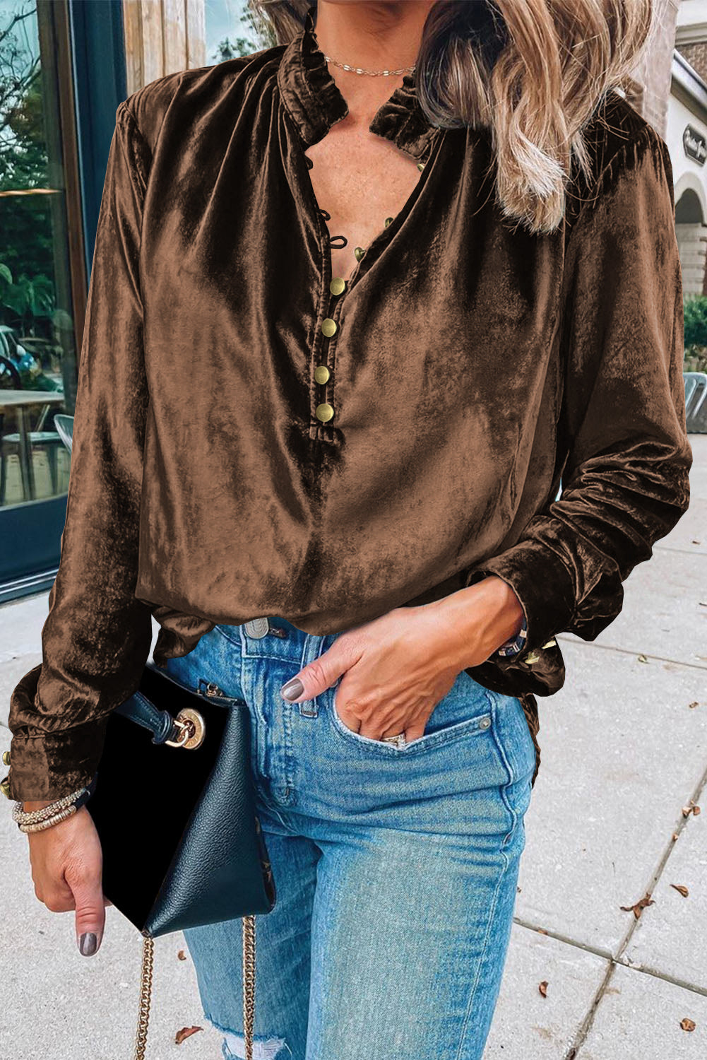 Person wearing a brown velvet shirt and blue jeans, holding a black handbag.