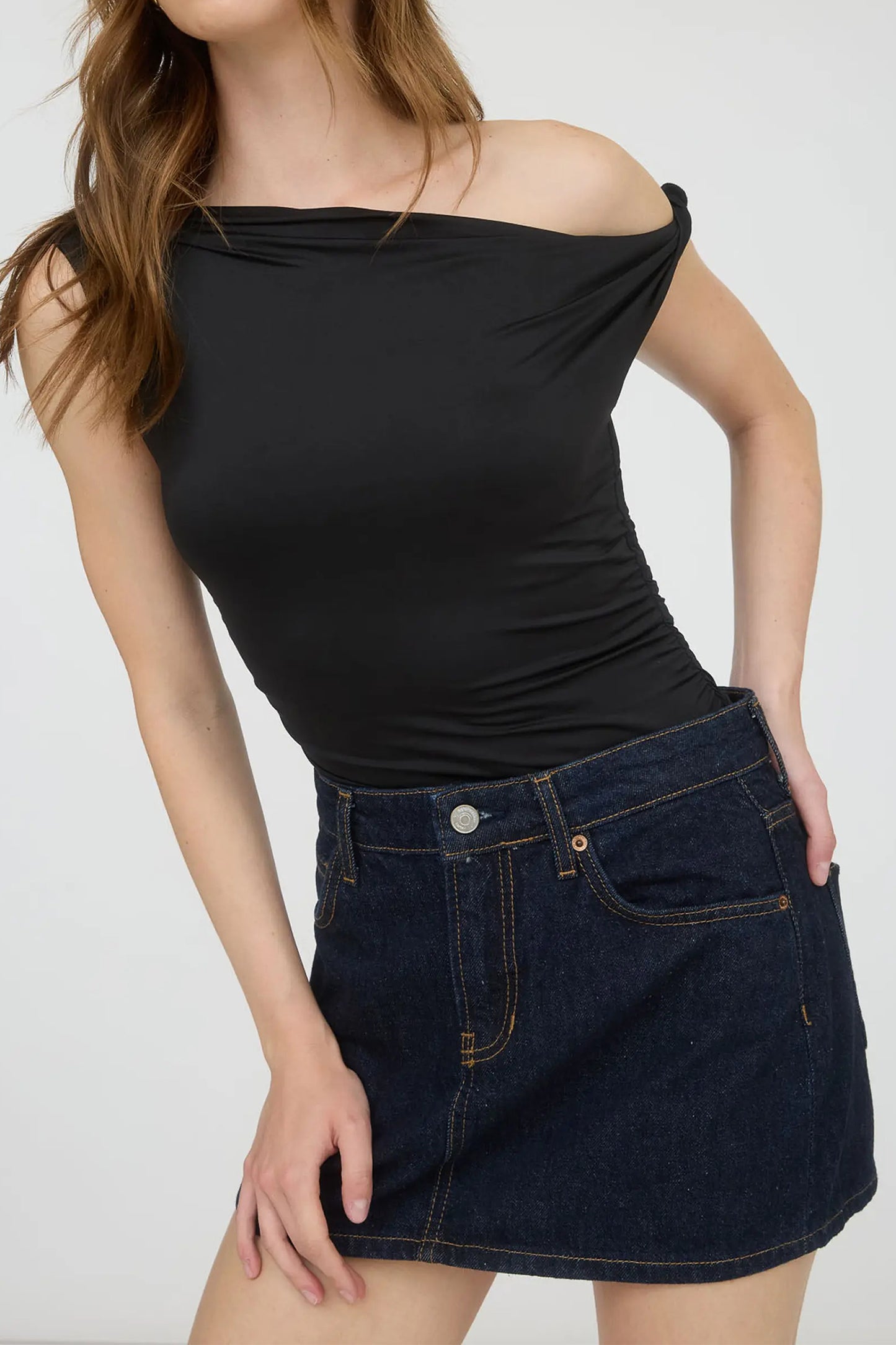Woman wearing a black off-shoulder top and denim skirt on a white background