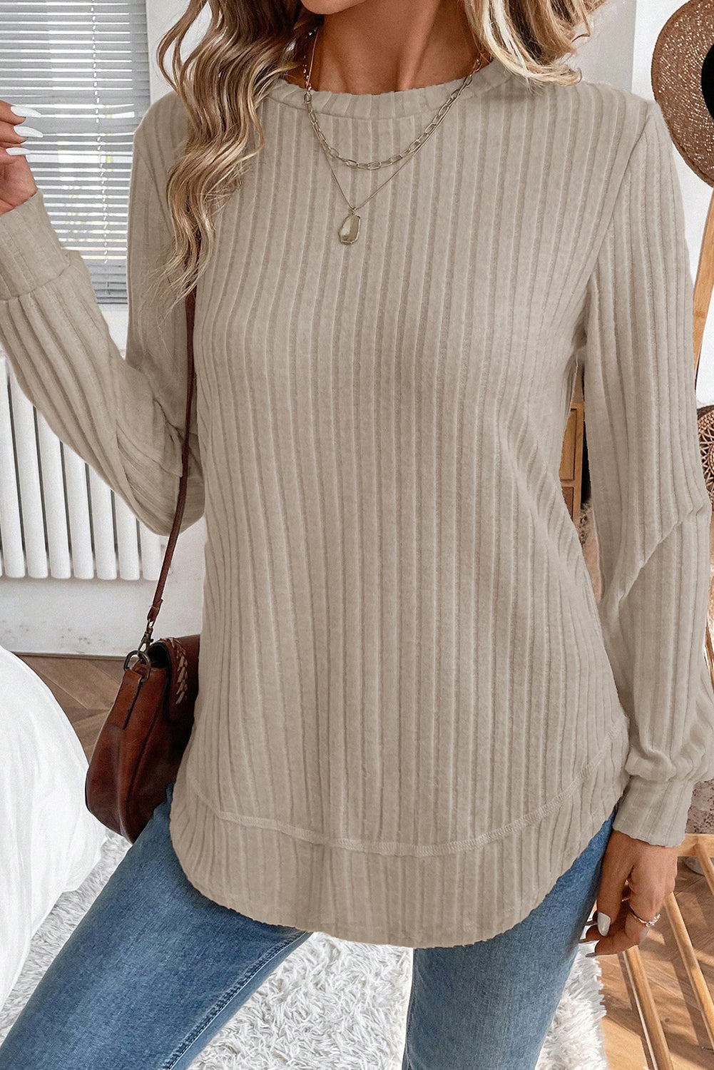 Person wearing a beige ribbed sweater and blue jeans indoors.