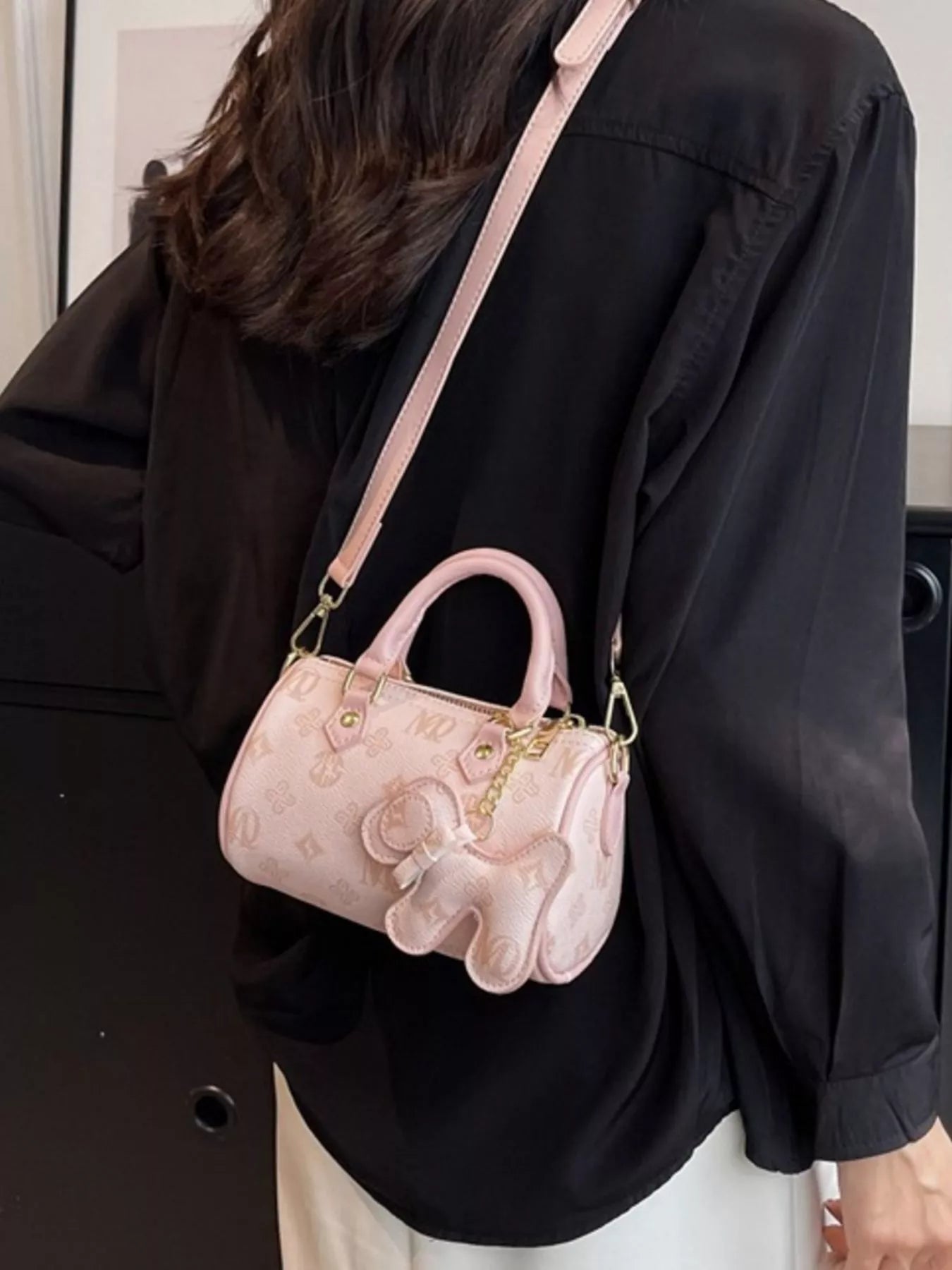 Person wearing a black jacket with a pink handbag featuring a cartoon character on a plain background