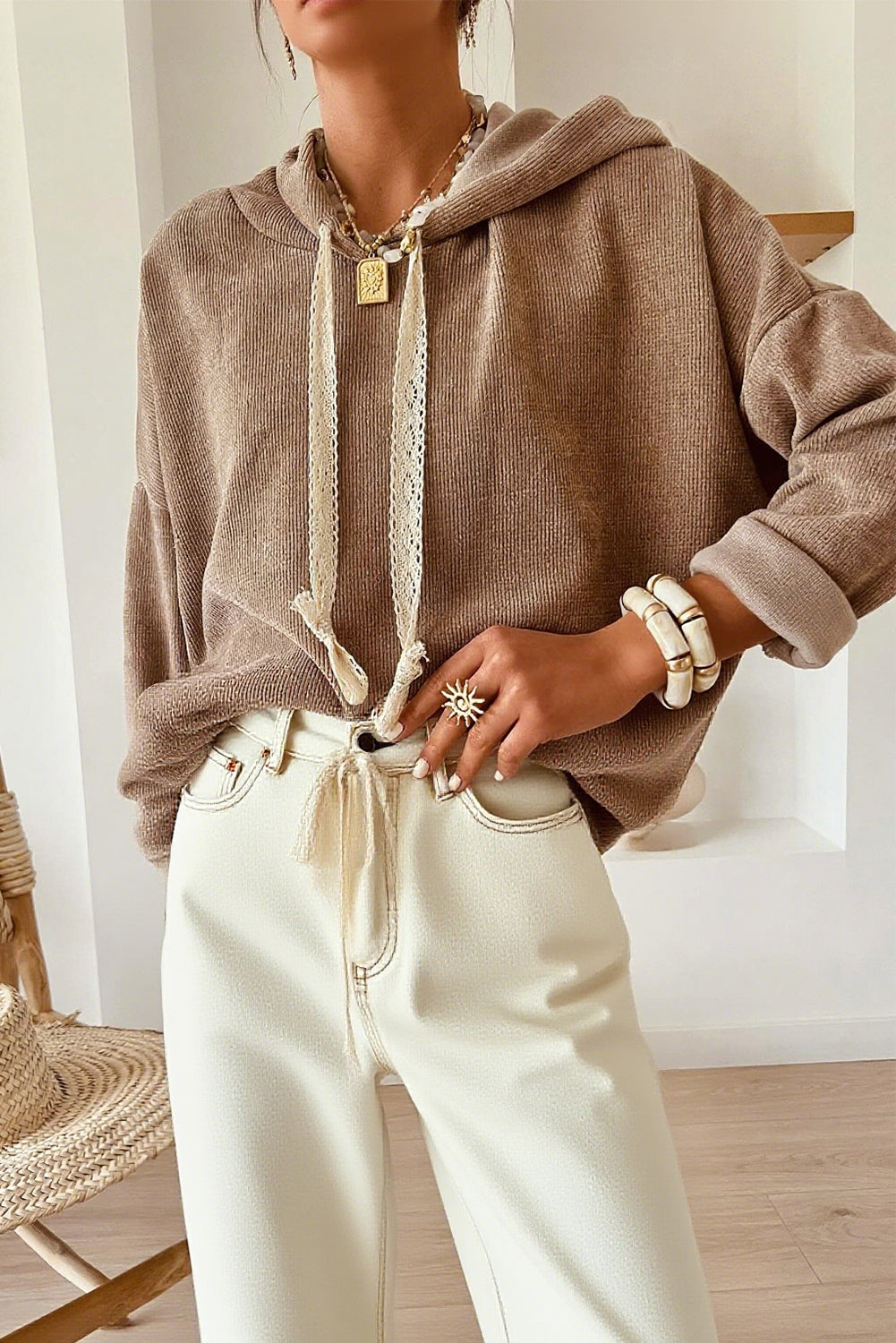 Person wearing a brown hoodie and white pants indoors.