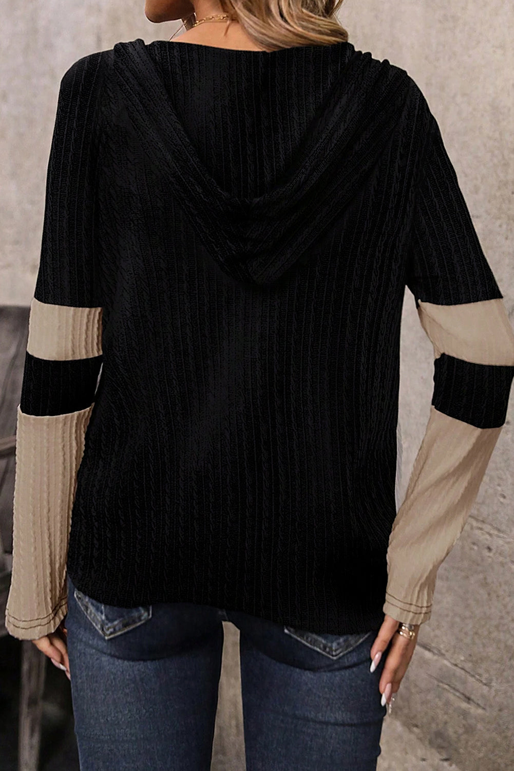 Black ribbed sweater with beige sleeves worn by a person against a neutral background