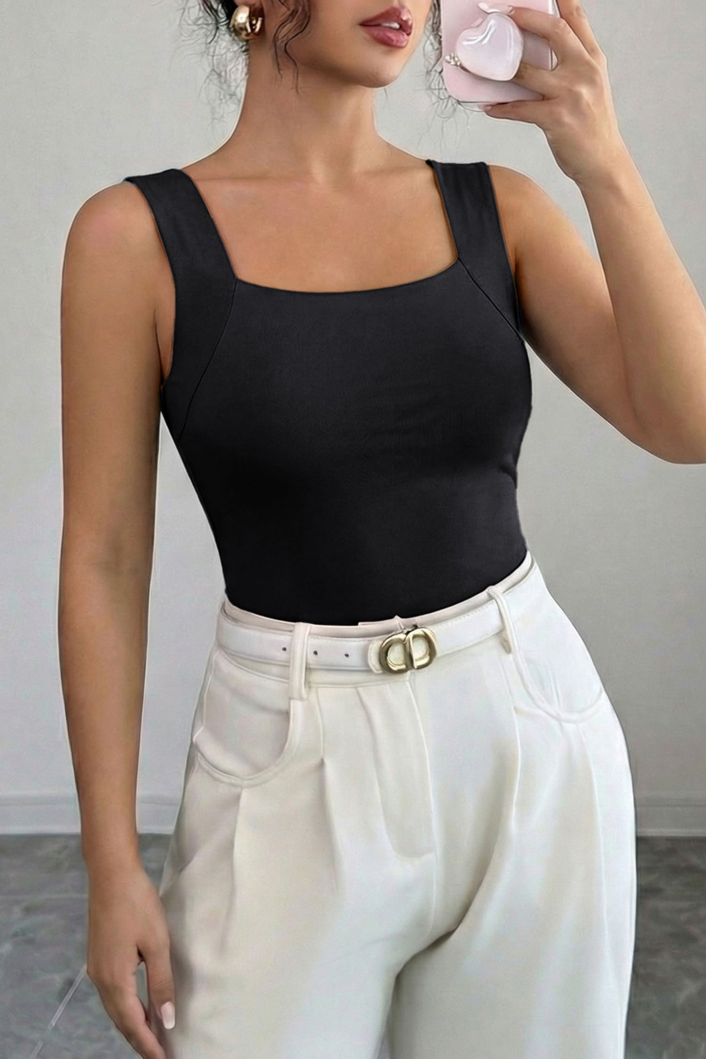 Person wearing a black tank top and white pants with a gray background