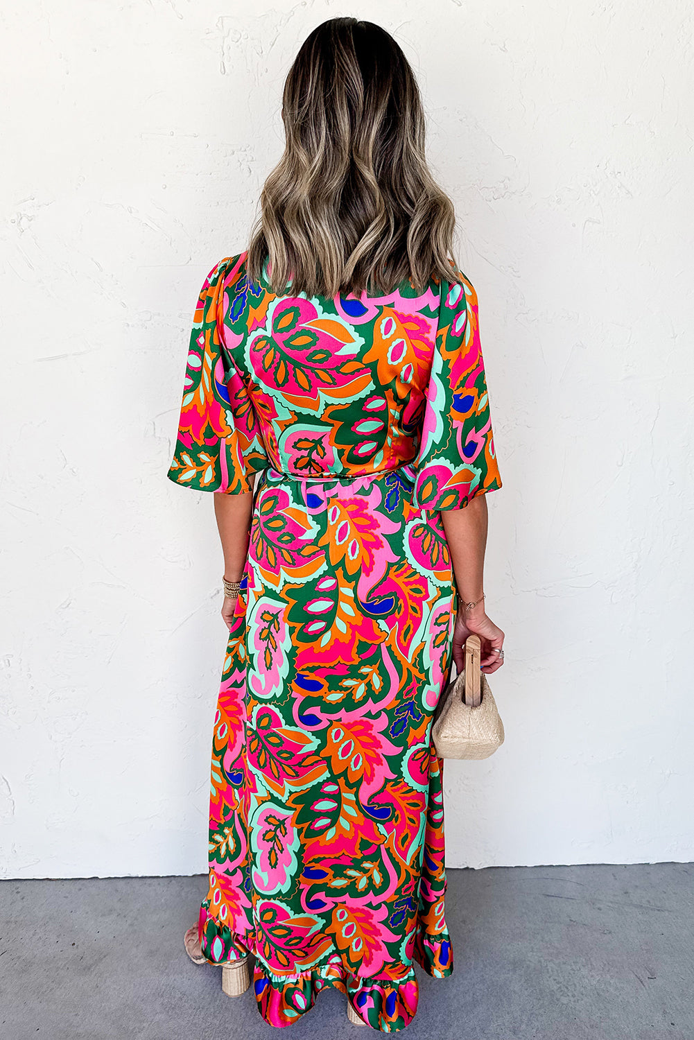 Woman wearing a colorful patterned dress back view against a white wall