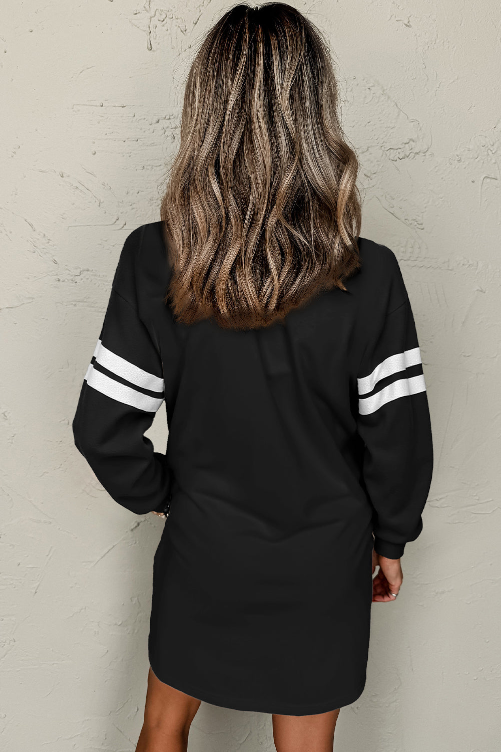 Back view of a model in an black colorblock athletic dress showcasing long sleeves and sporty stripes,