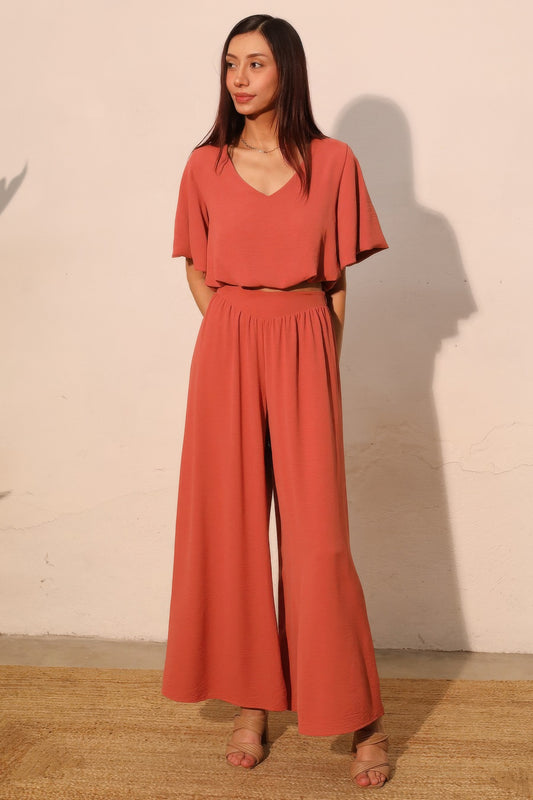 Woman wearing a coral jumpsuit standing against a plain wall. Front view