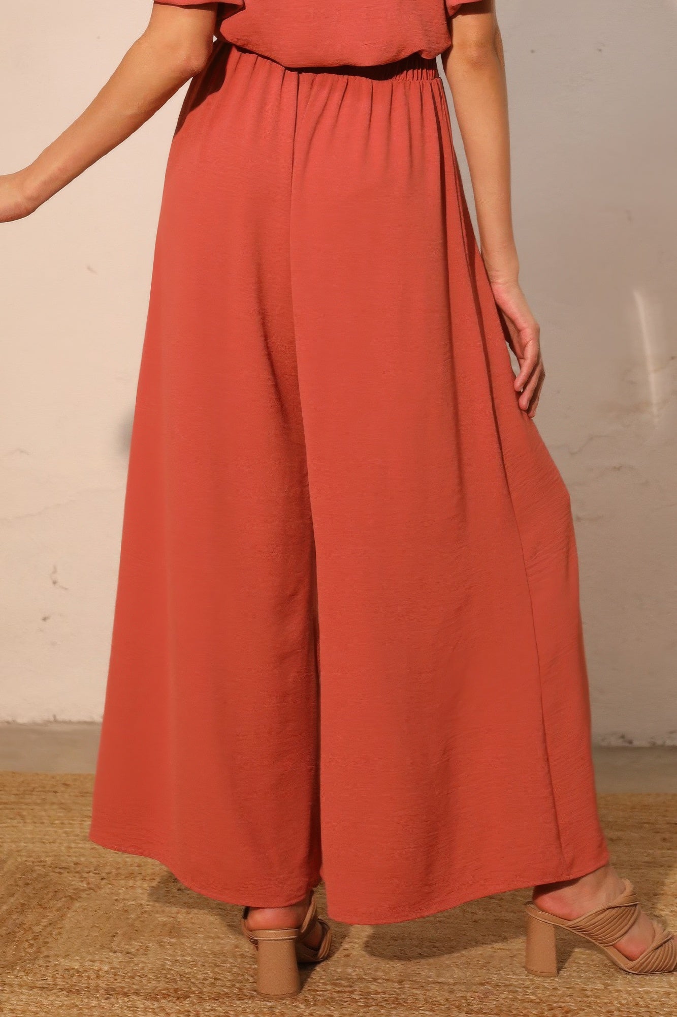 Person wearing a rust-colored outfit with wide-leg pants against a neutral background back view