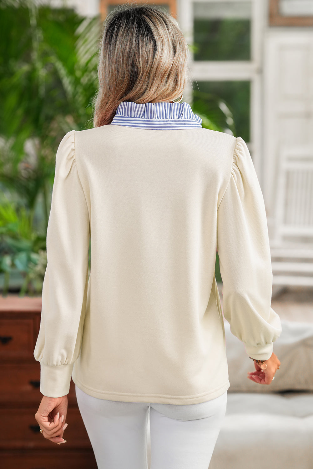 Woman wearing a beige blouse with long sleeves and a striped collar in an outdoor setting.