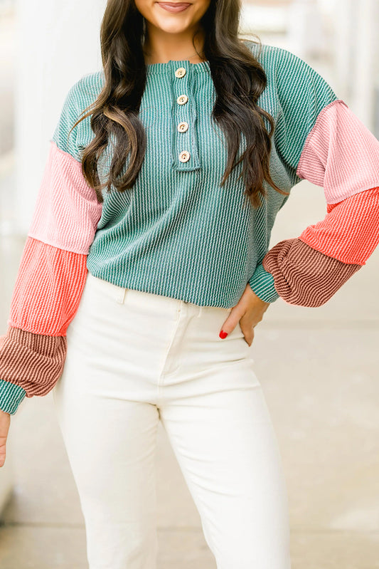 Close-up of a model in a ribbed colorblock top with a button front and wide sleeves, featuring green, pink, and coral panels.