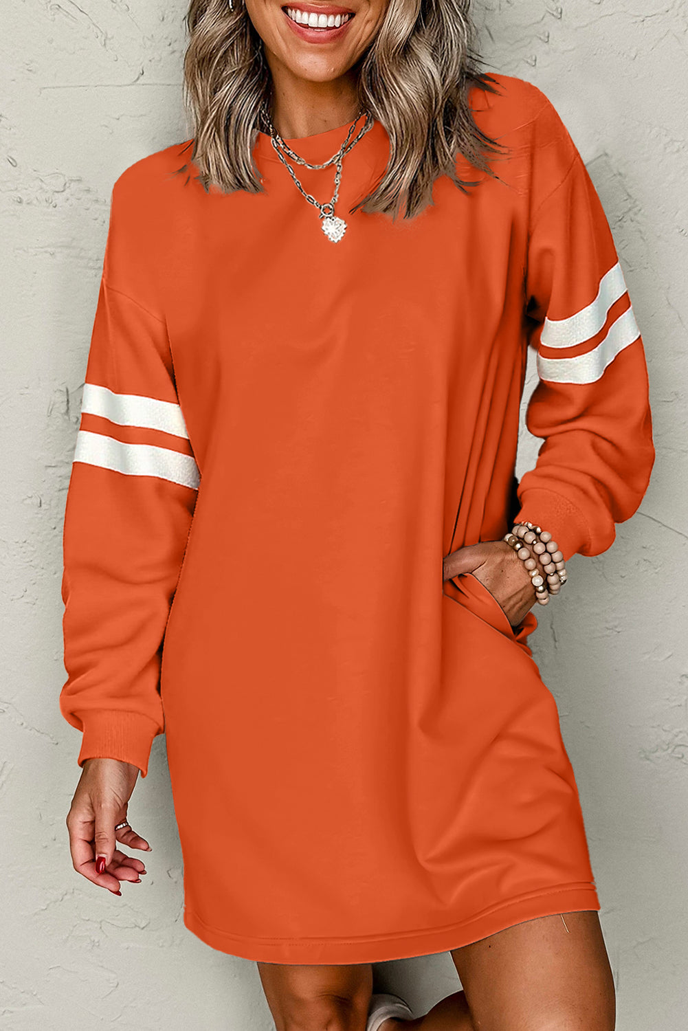 Close-up of a model in an orange athletic dress, featuring side pockets and sporty white stripes, posed playfully with a smile