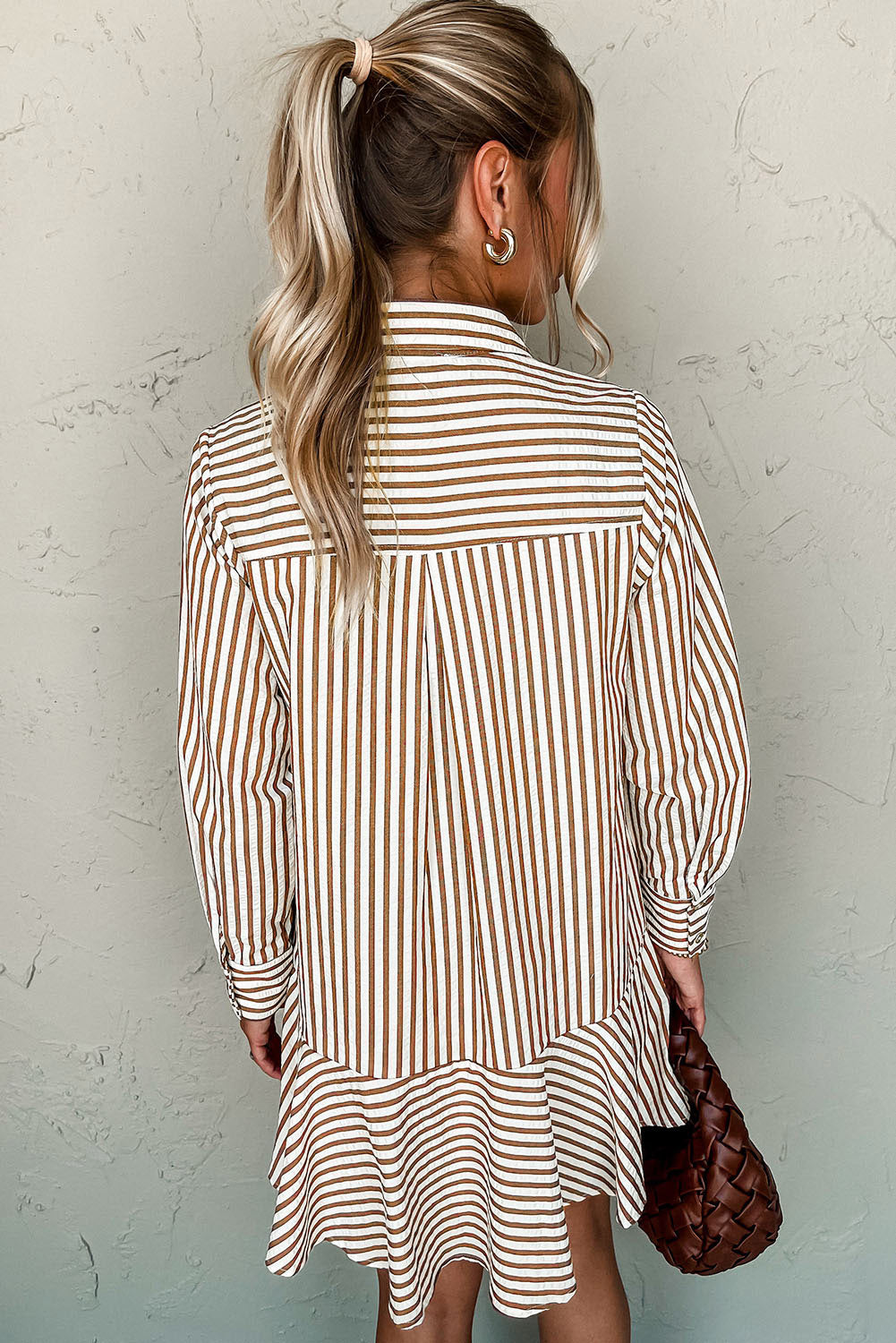 Woman wearing a striped shirt dress against a textured wall.