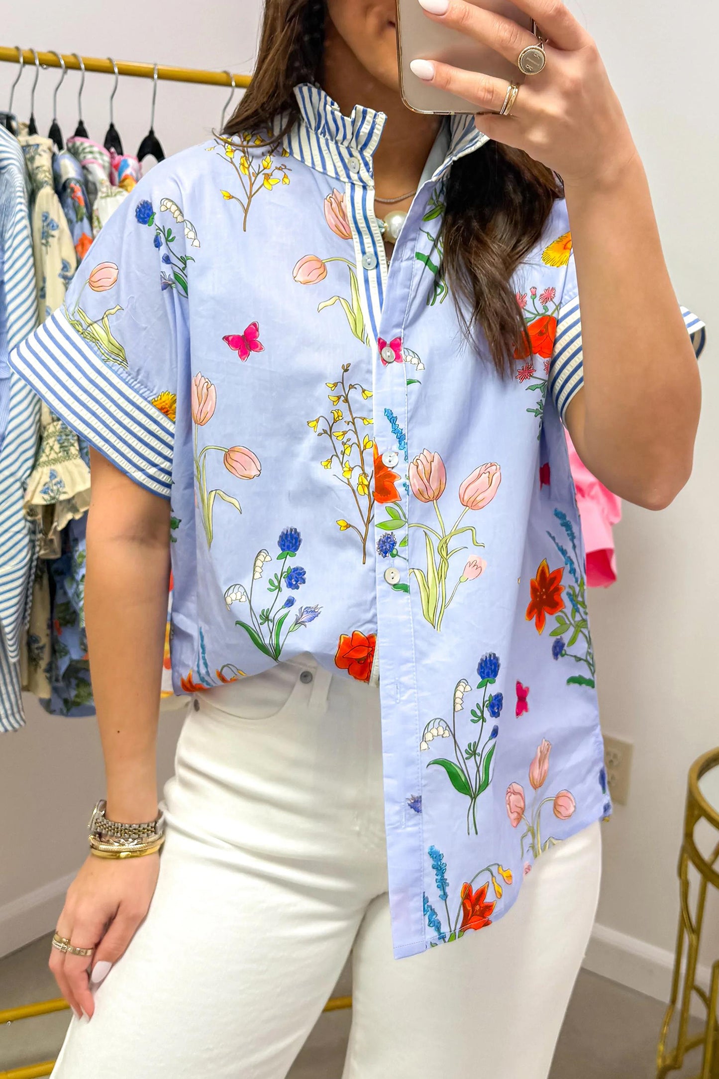 Person wearing a colorful floral shirt taking a mirror selfie in a clothing store.