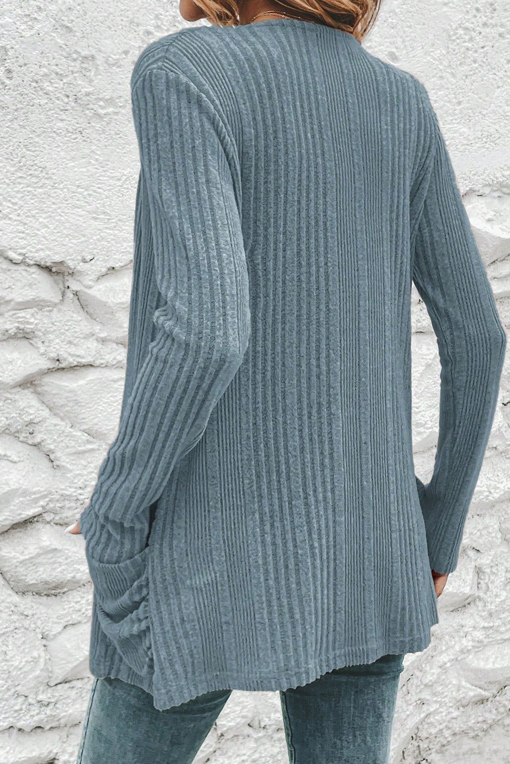 Person wearing a blue ribbed sweater against a stone wall.
