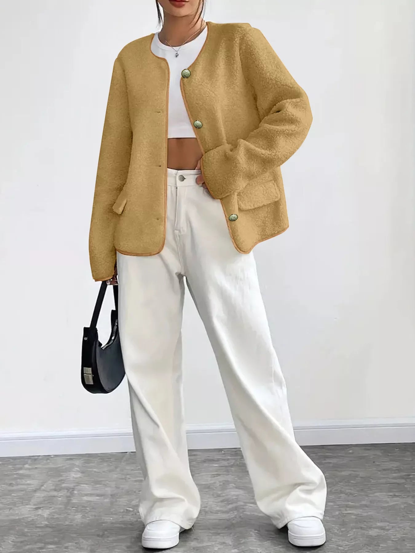 Person wearing a mustard yellow cardigan, white pants, and white sneakers with a black handbag.