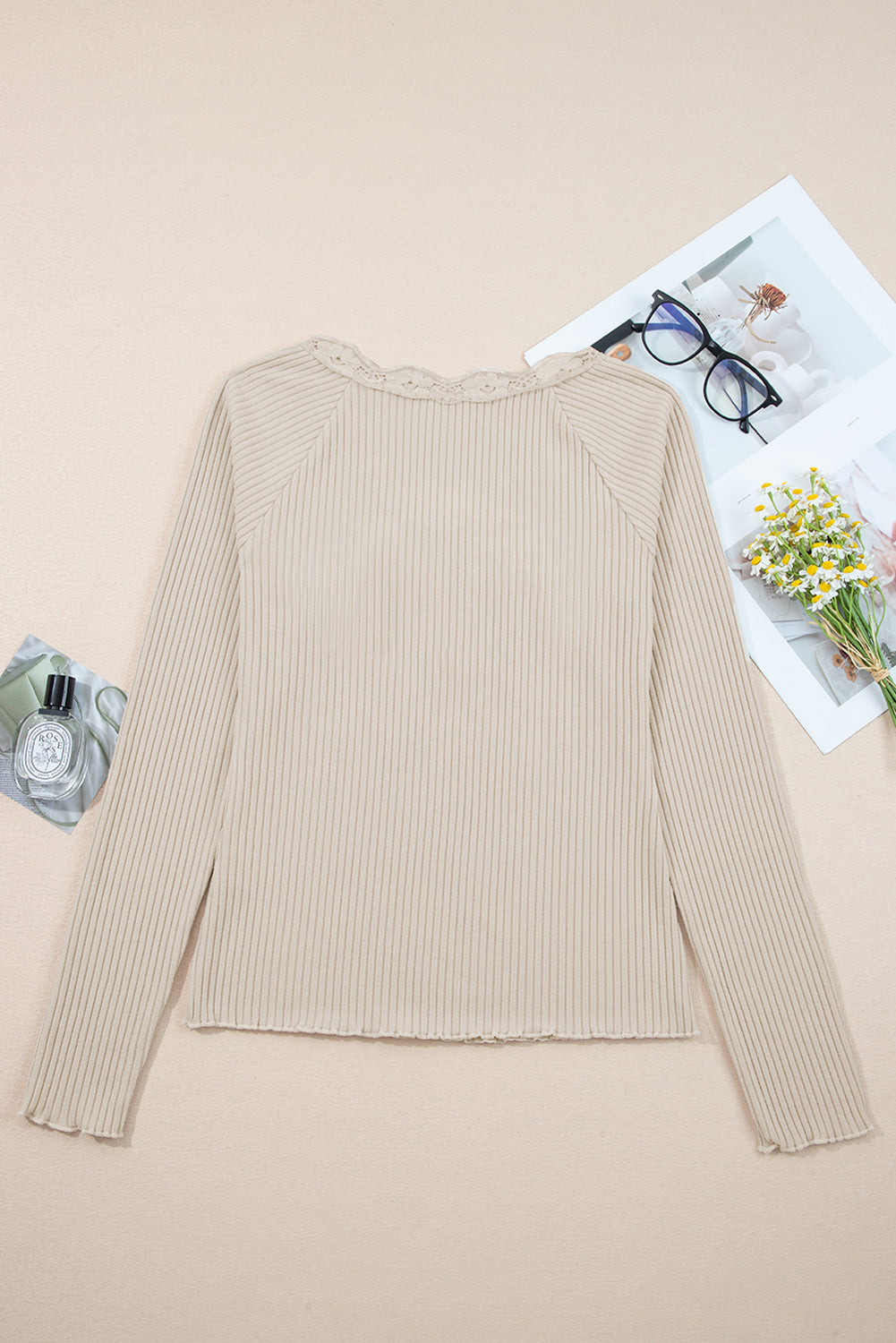 Beige ribbed long-sleeve top on a beige background with glasses and flowers.