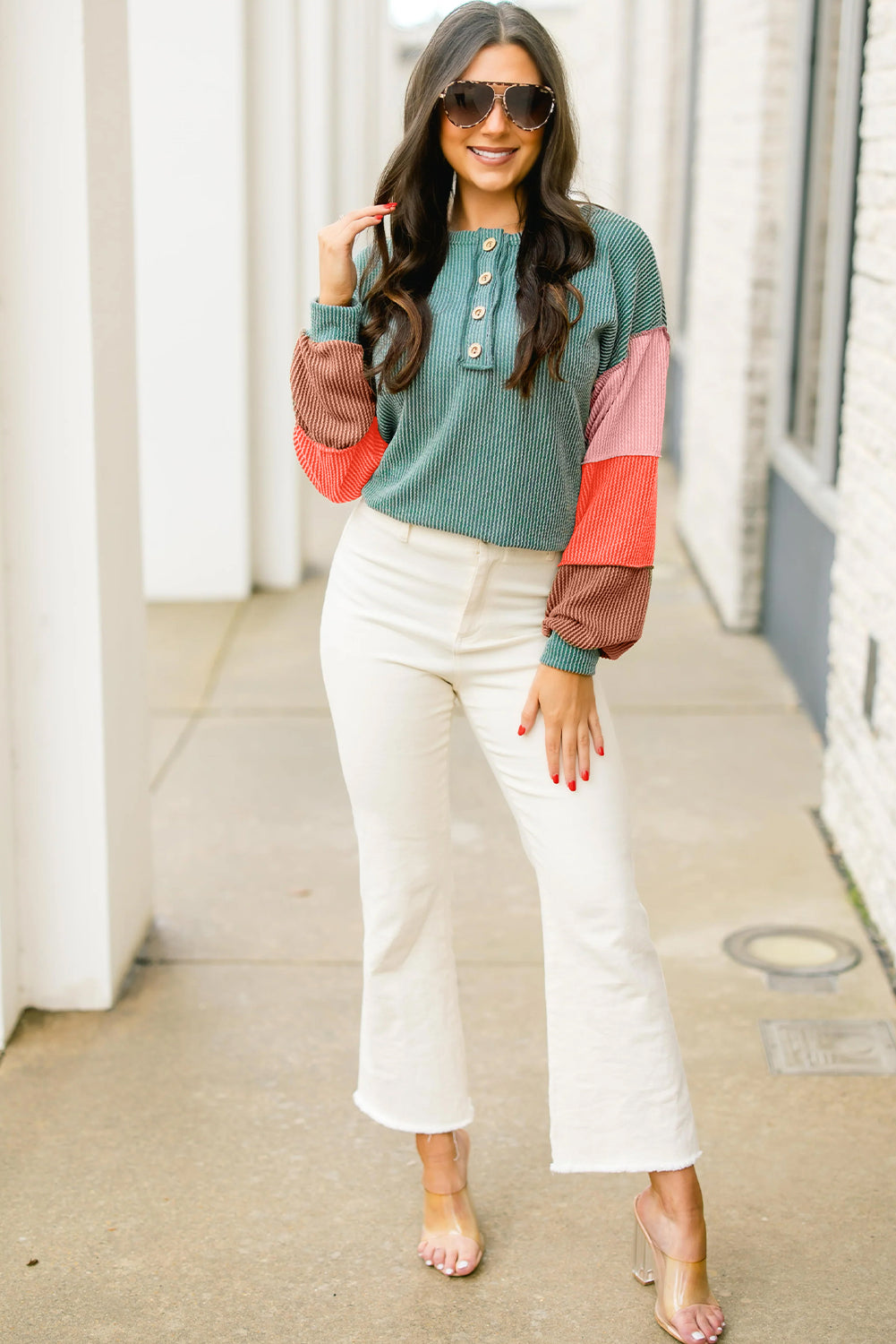 Model posing in a trendy colorblock top, showing a relaxed fit with colorful sleeves paired with white high-waisted pants.