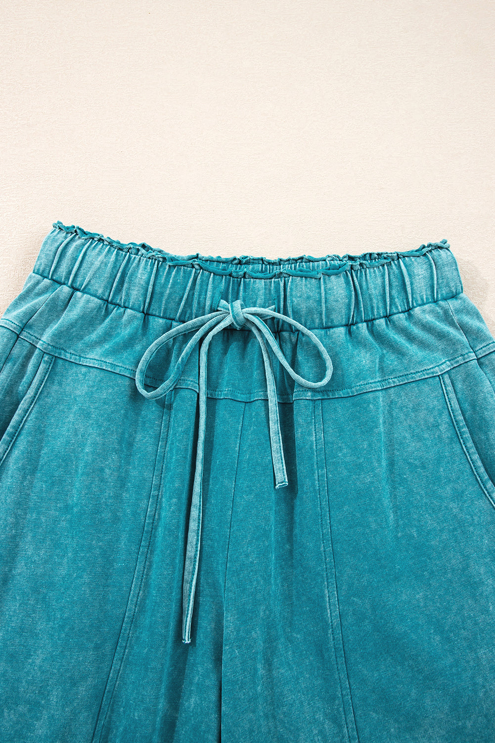 Teal pants with drawstring waist on a beige background