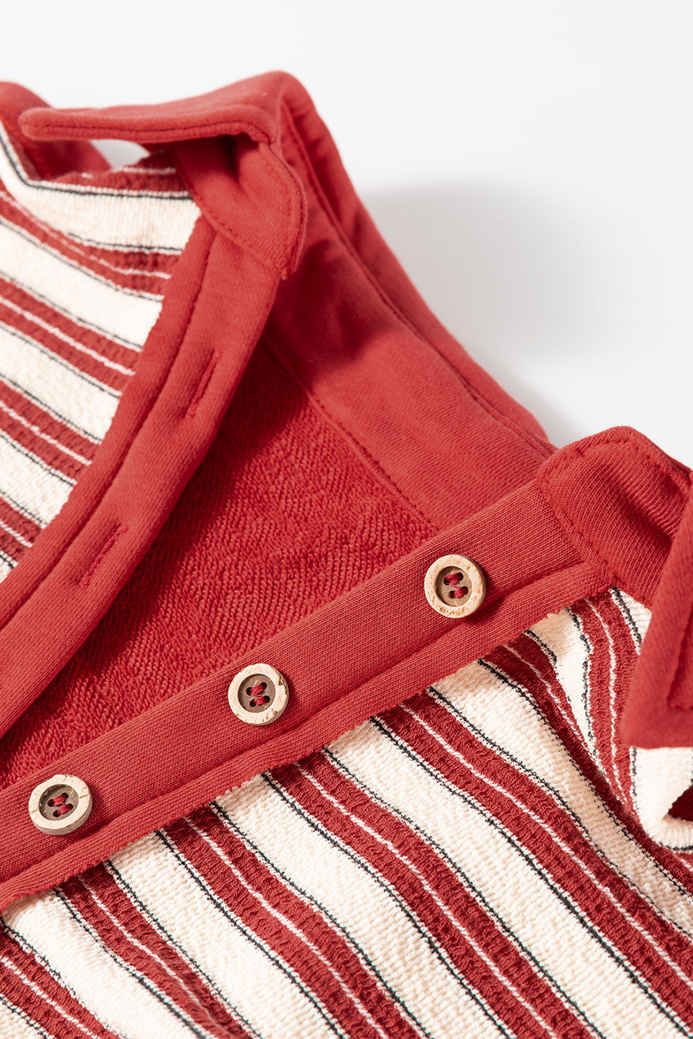 Close-up of a red and white striped baby outfit with buttons on a white background