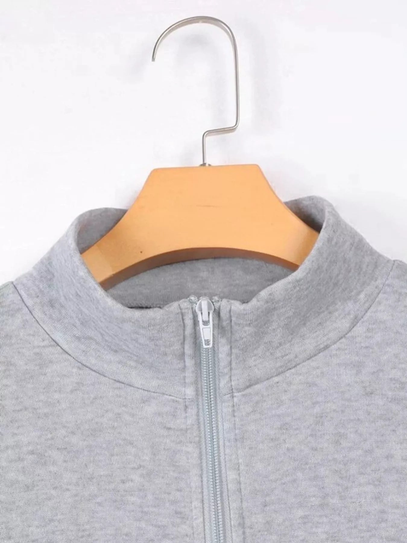 Gray zip-up hoodie on a wooden hanger against a white background