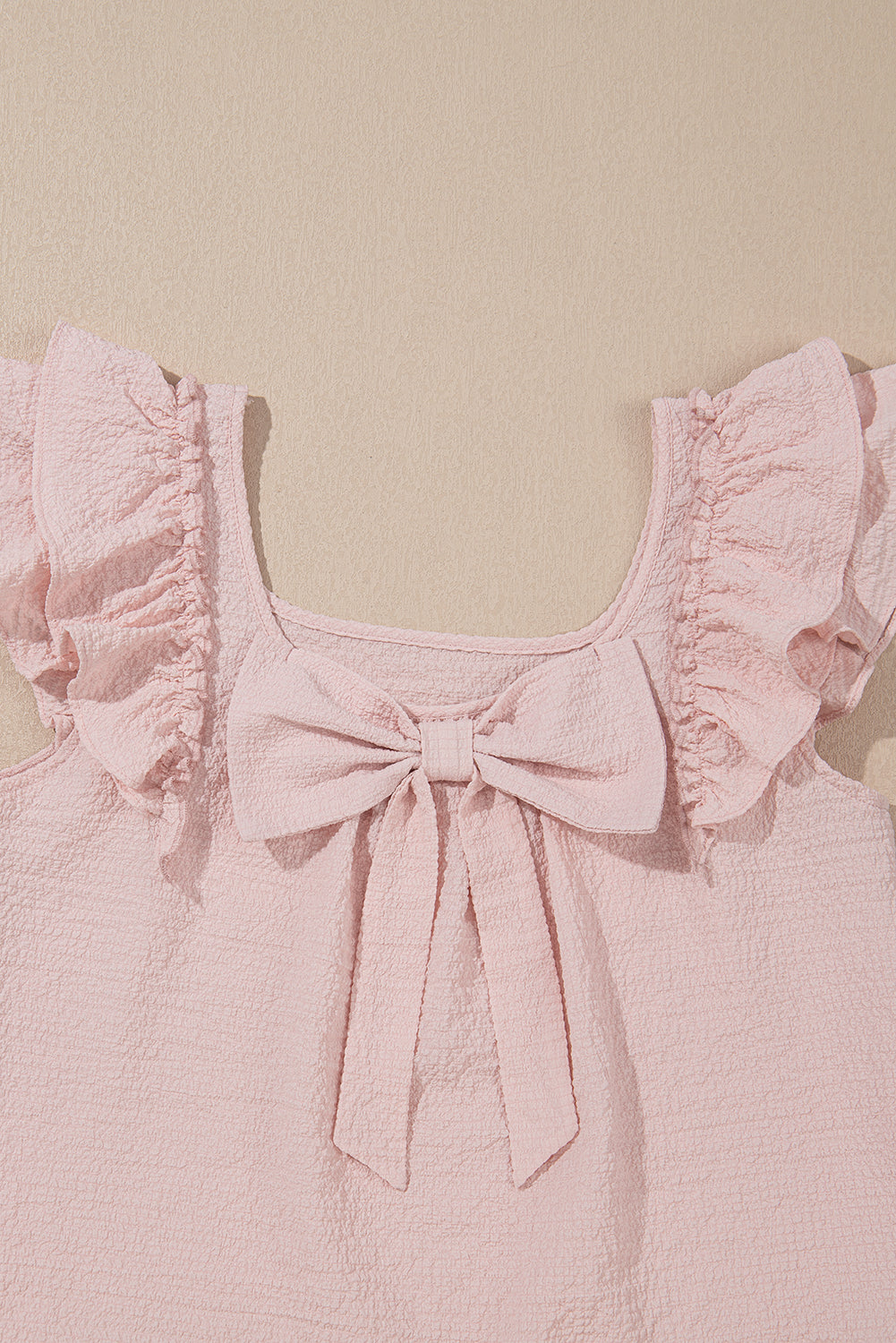 Pink top with ruffled sleeves and a bow detail on a beige background