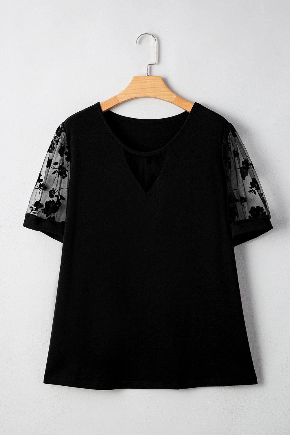 Black blouse with floral sleeves on a wooden hanger against a white background