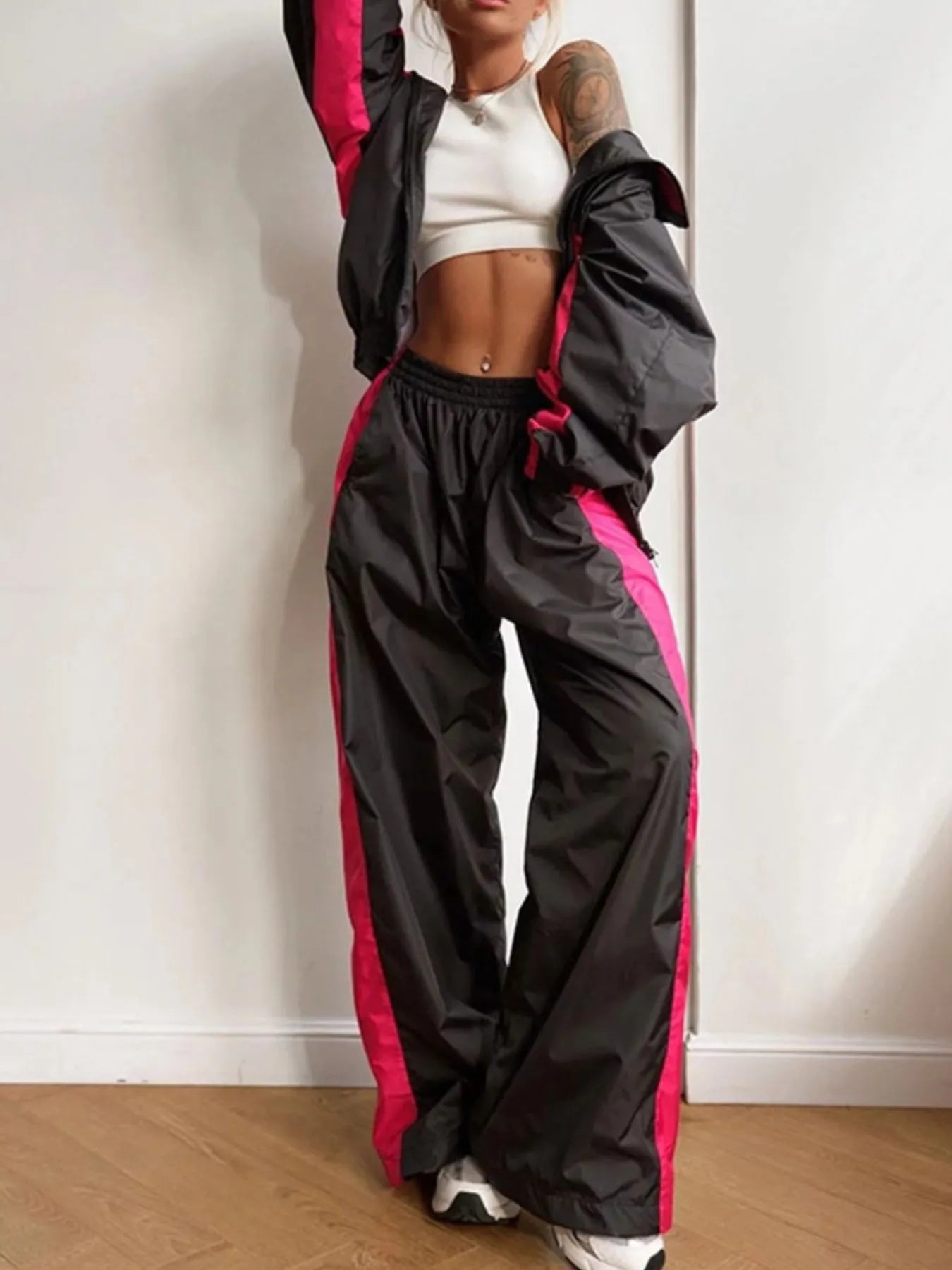 Person wearing a black and pink tracksuit against a white wall.
