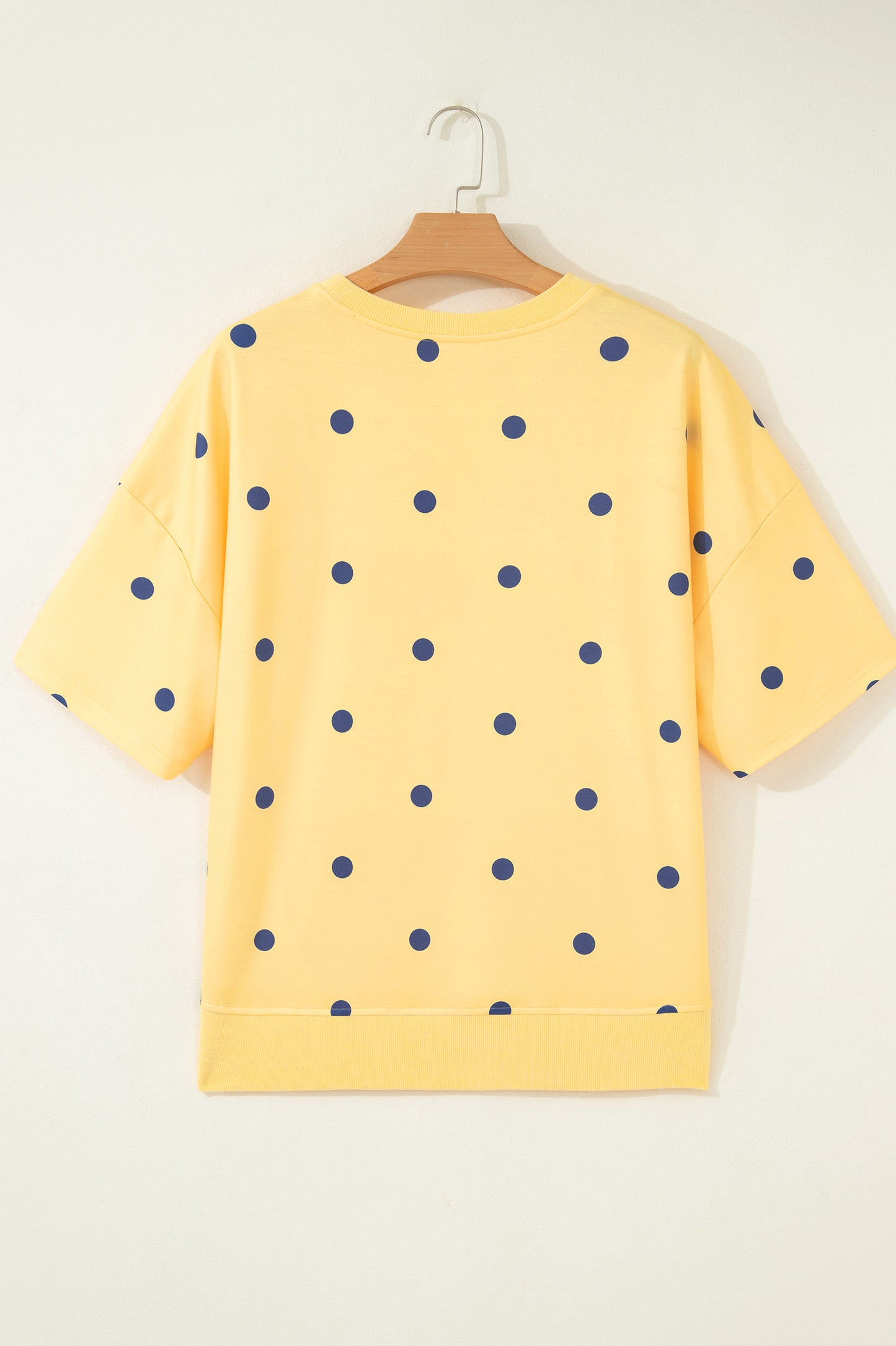 Yellow sweatshirt with blue polka dots on a hanger against a white background. Back