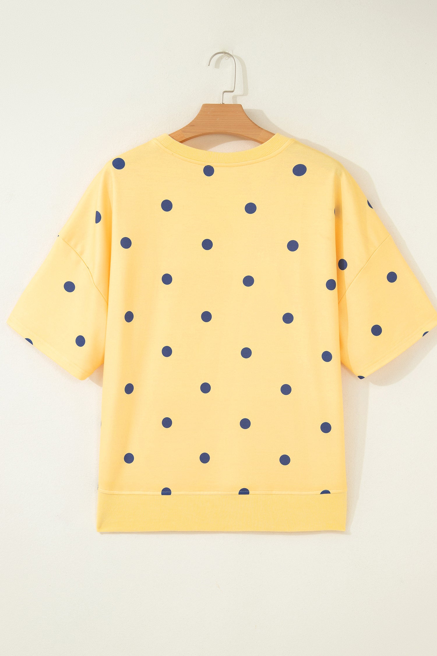 Yellow sweatshirt with blue polka dots on a hanger against a white background. Back