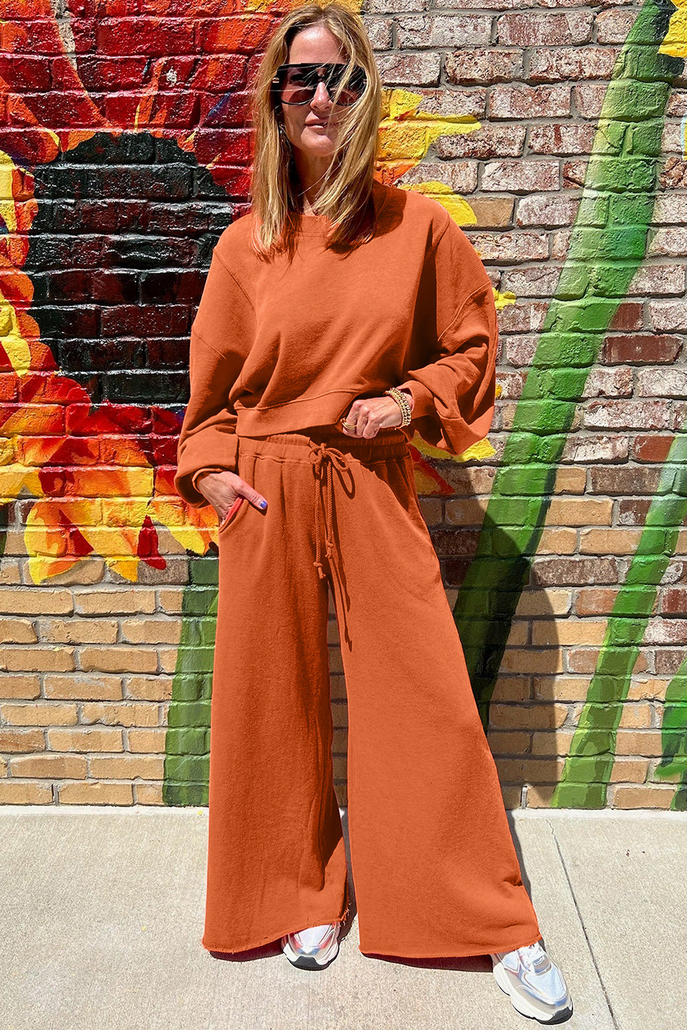Woman in an orange outfit standing in front of a colorful mural.