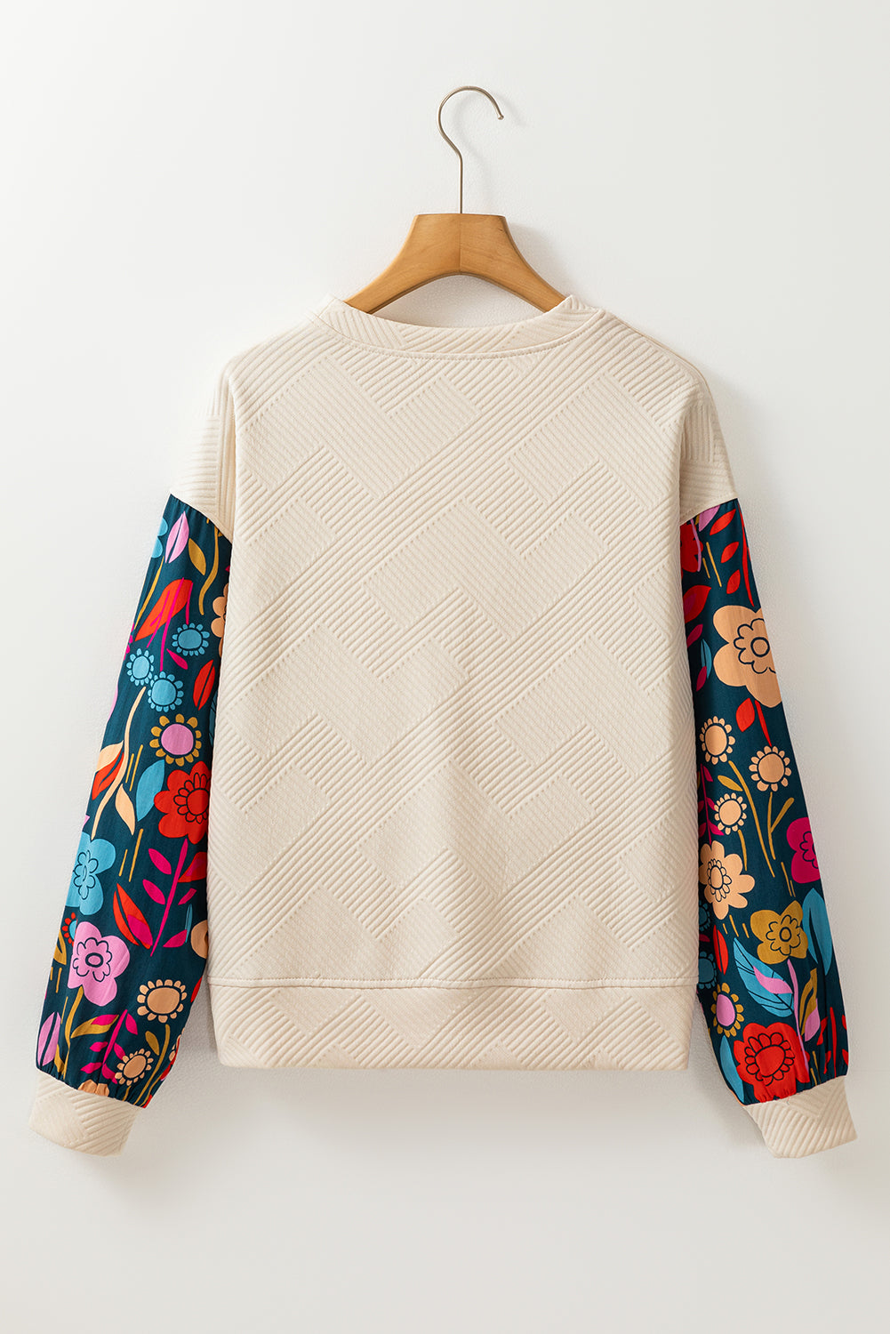 Beige sweatshirt with colorful floral sleeves on a wooden hanger against a white background