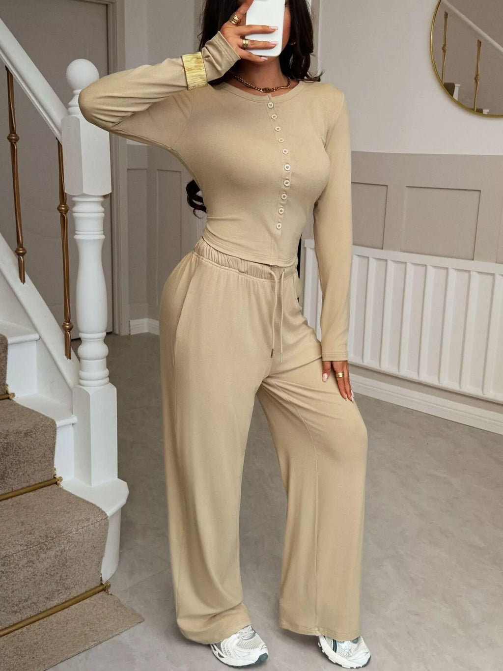 Person wearing a beige outfit taking a mirror selfie in a home setting.