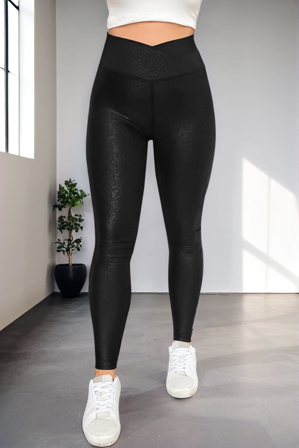 Person wearing black leggings and white sneakers in a minimalistic room with a plant.