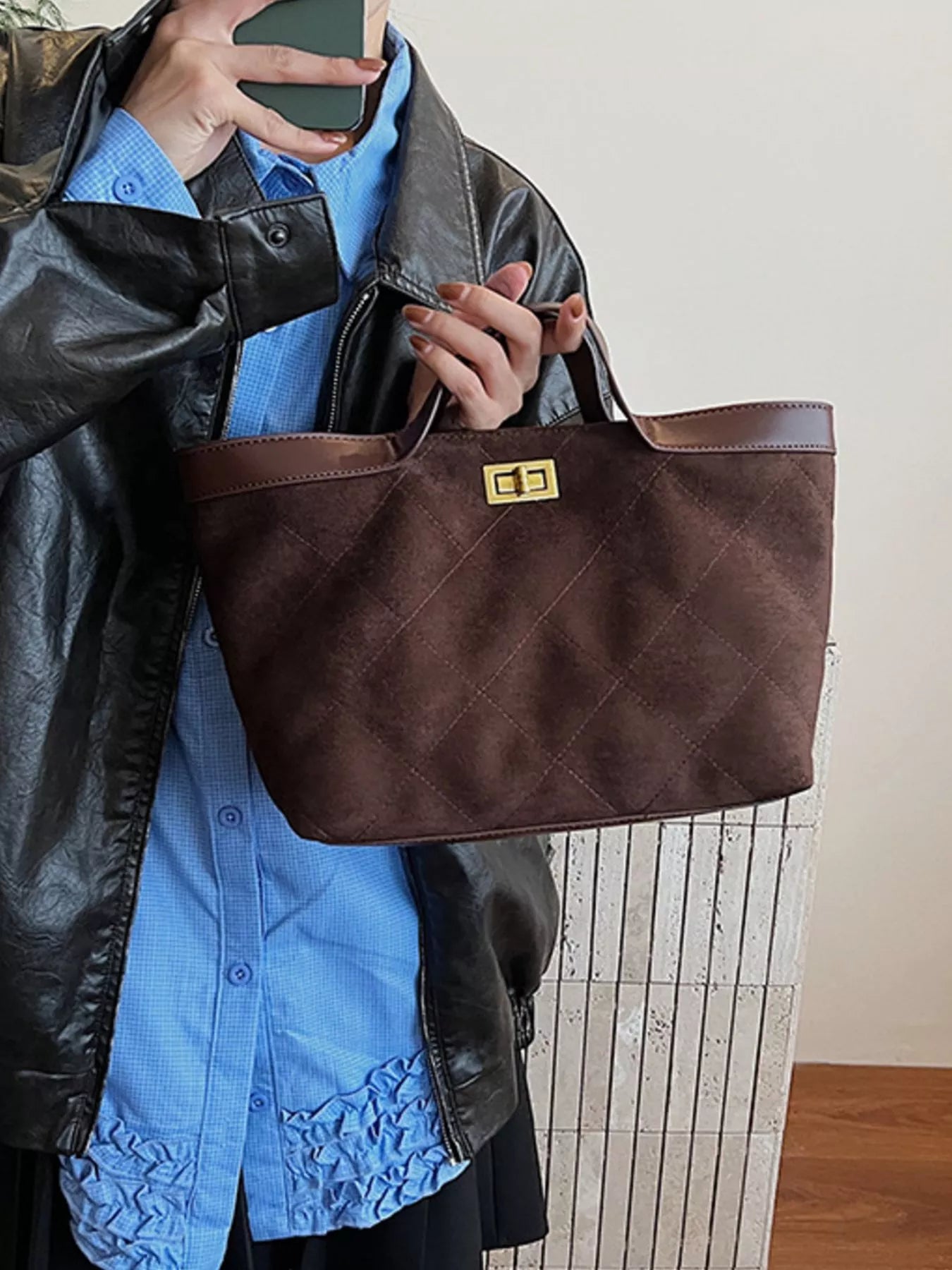 Person holding a brown quilted handbag with a gold clasp.