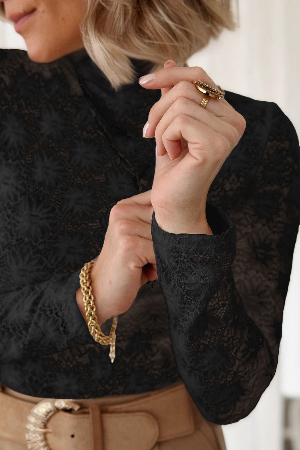 Person wearing a black lace top with gold jewelry on a blurred background