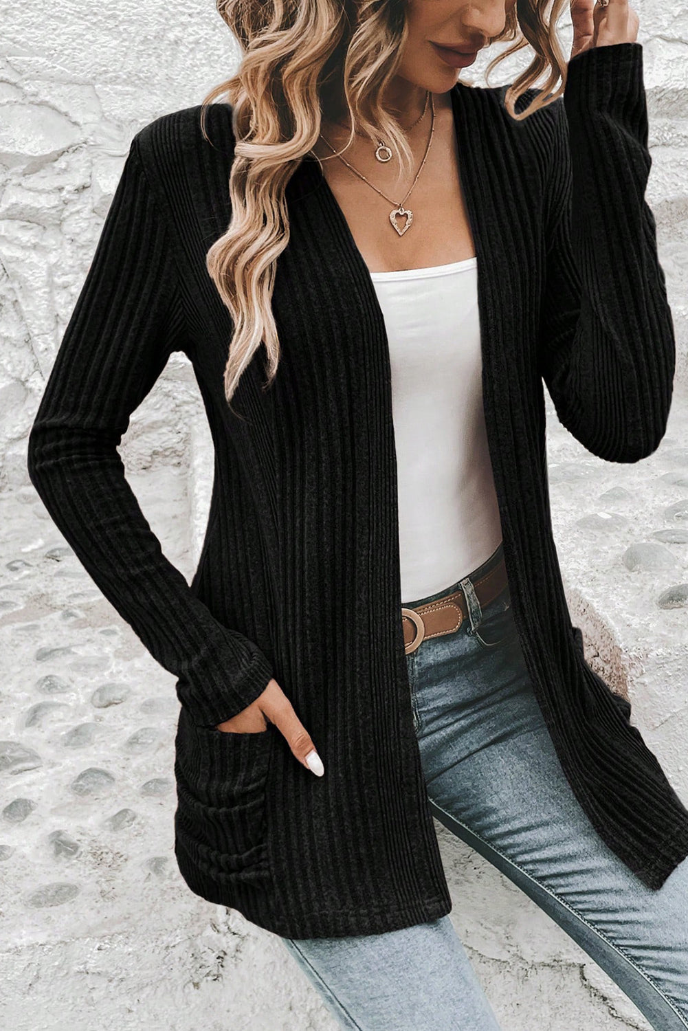 Person wearing a black ribbed cardigan over a white top and blue jeans.
