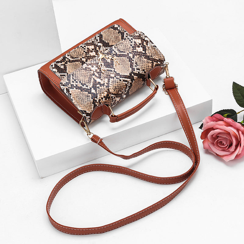 Snake print handbag with brown strap on a white surface with a pink rose.