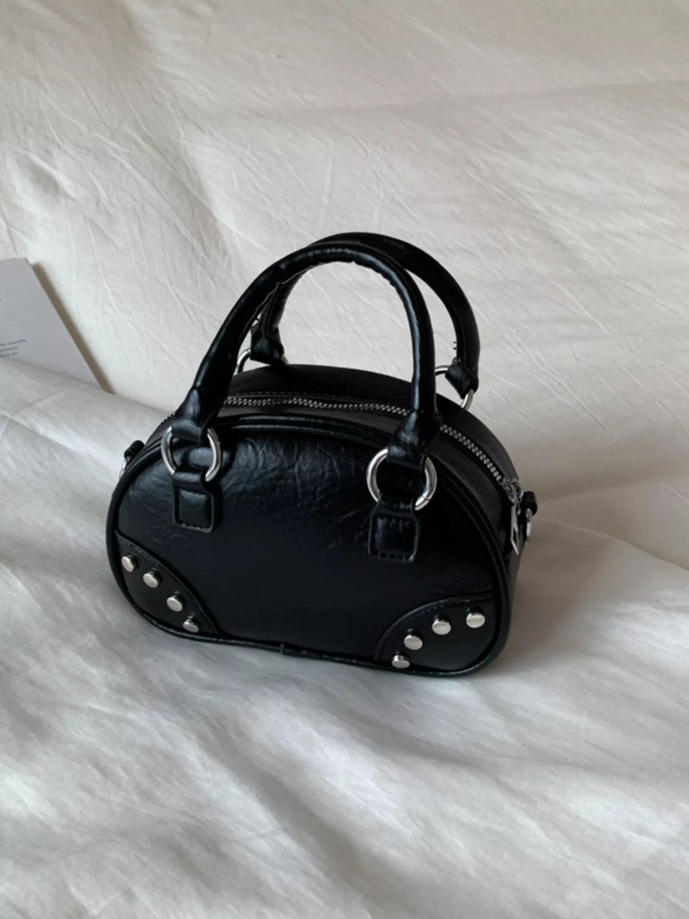 Black handbag with studs on a white fabric background