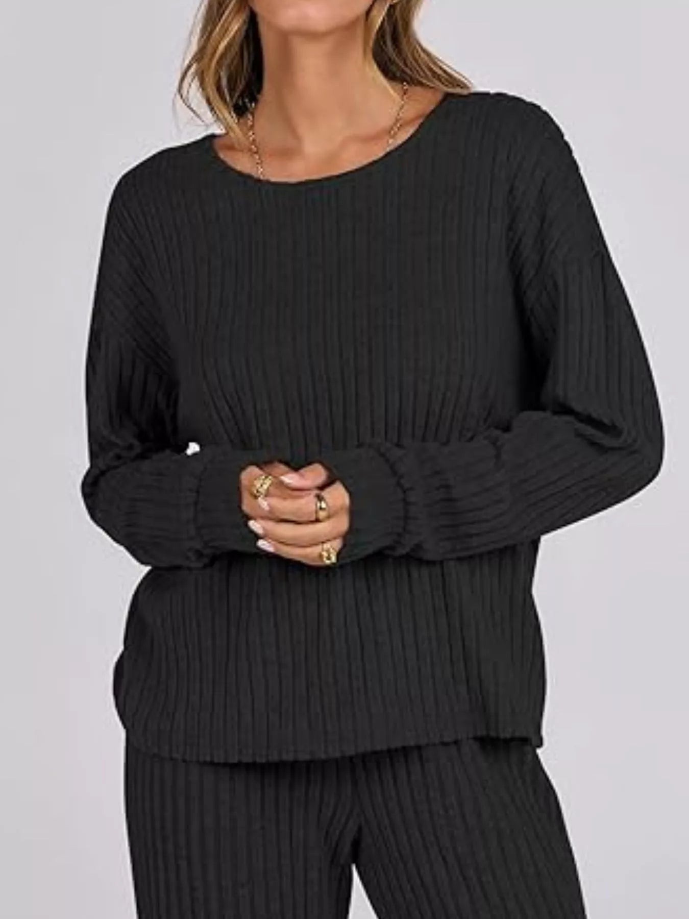 Person wearing a black ribbed sweater and pants on a plain background