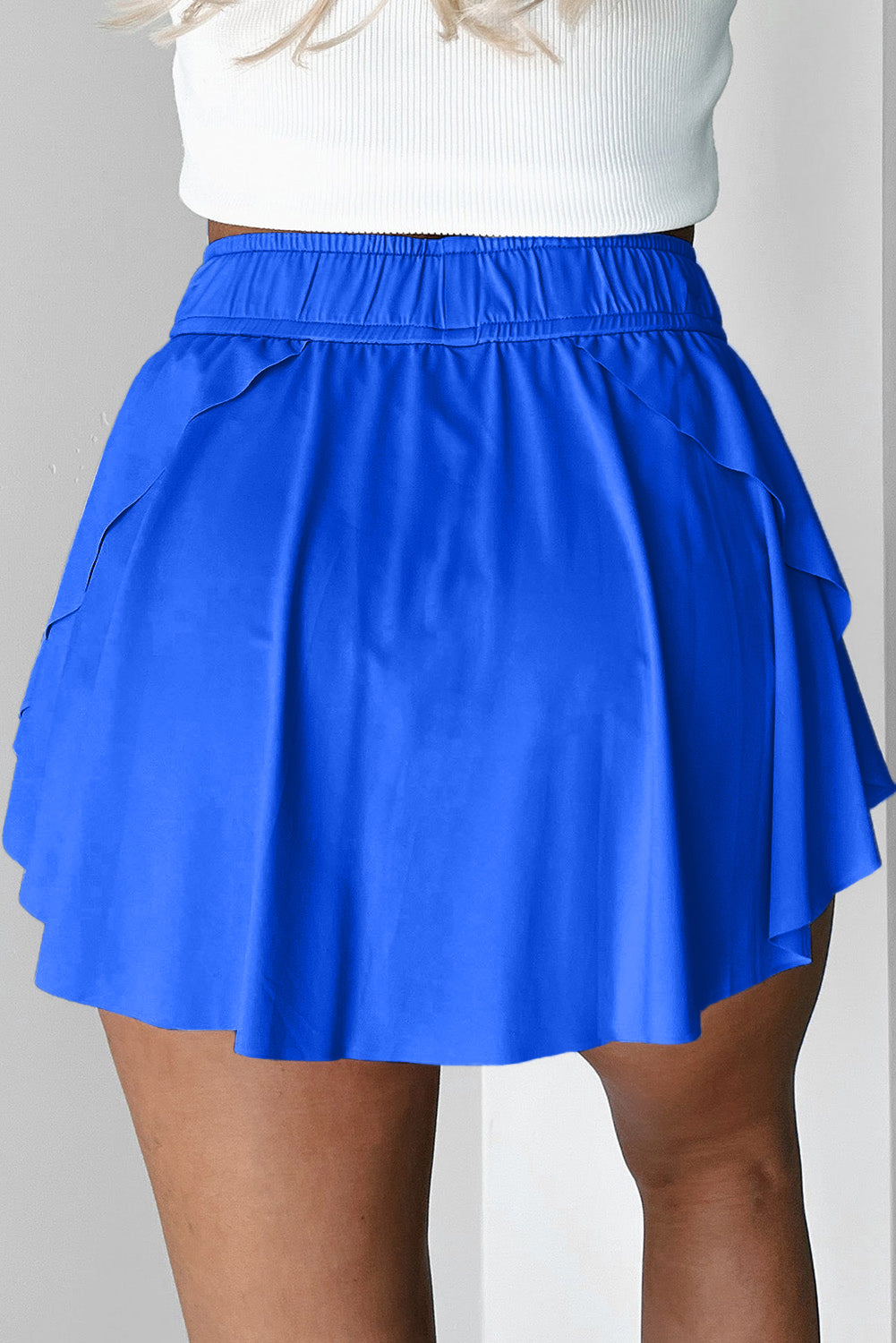 Blue tennis skirt worn over a white top on a plain background back view 