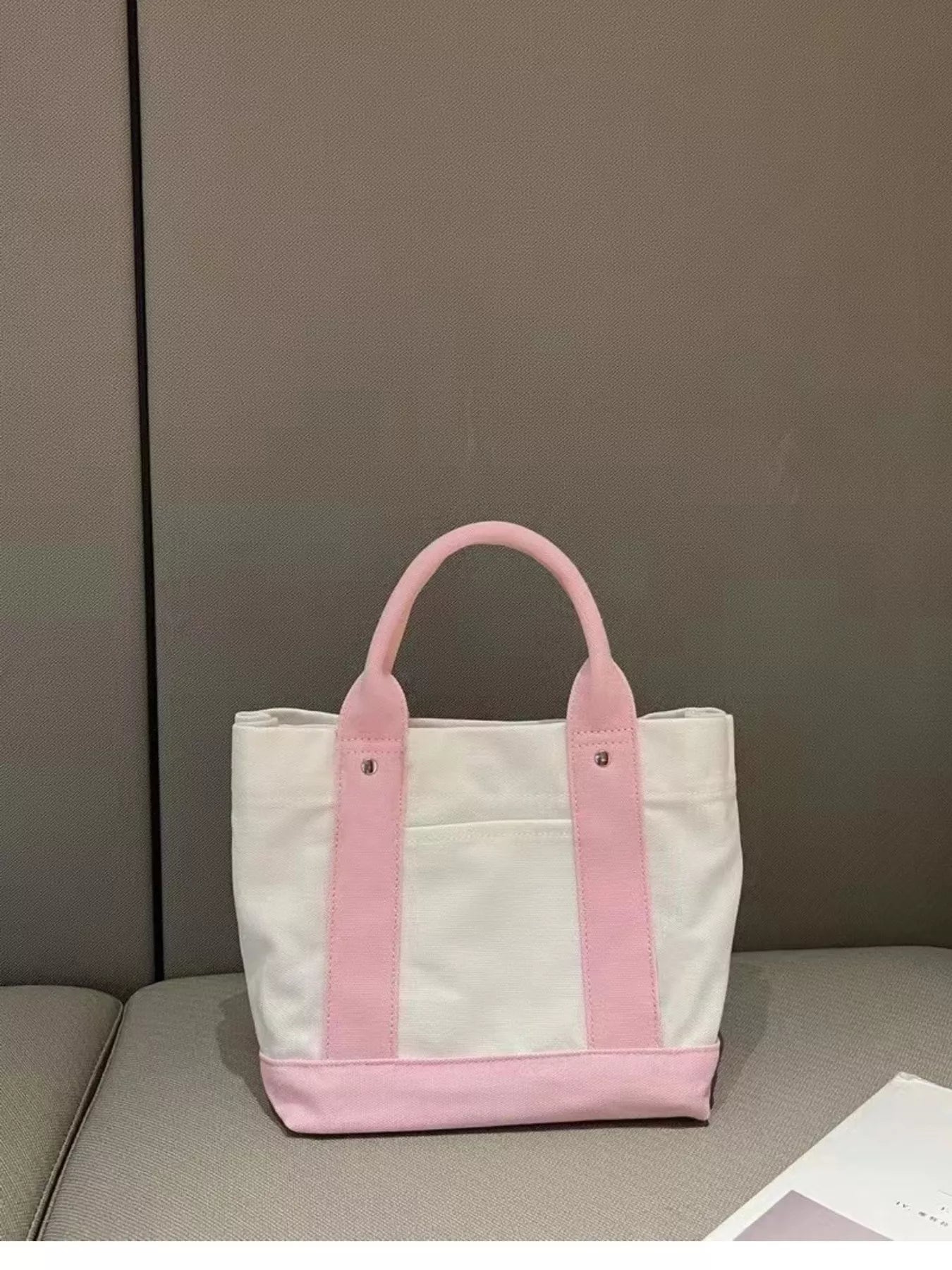 White tote bag with pink handles on a gray surface against a gray background