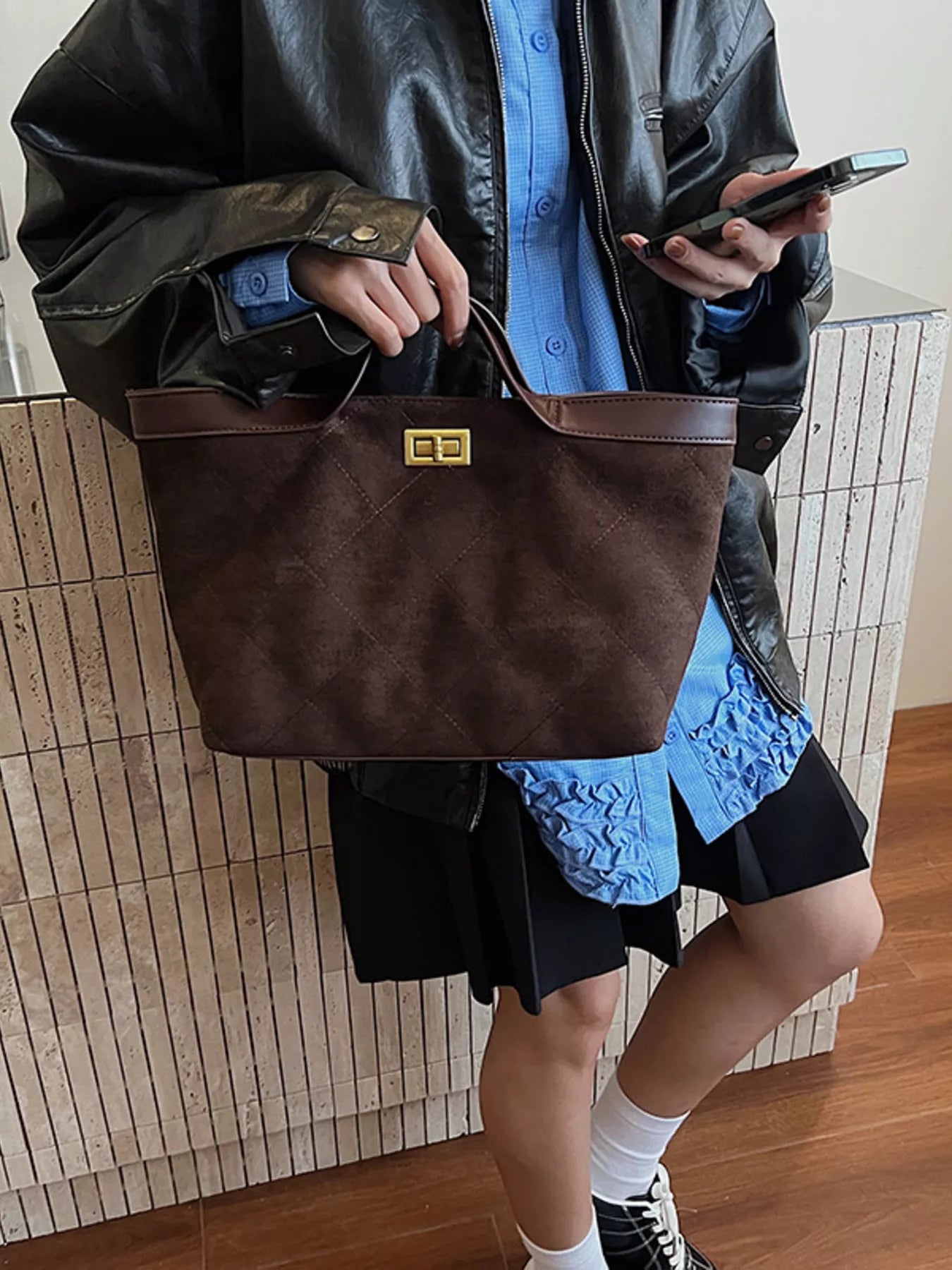 Person holding a brown leather bag with a textured wall background