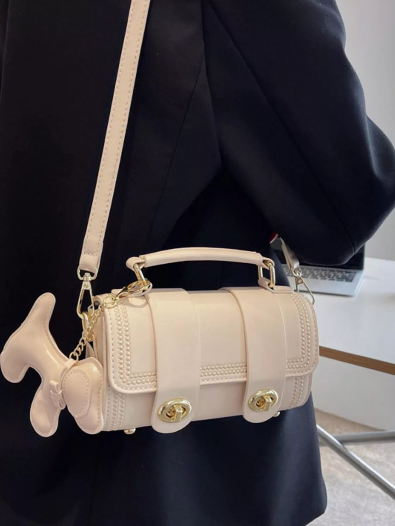 Beige fish-shaped handbag with gold accents worn by a person in a dark outfit.