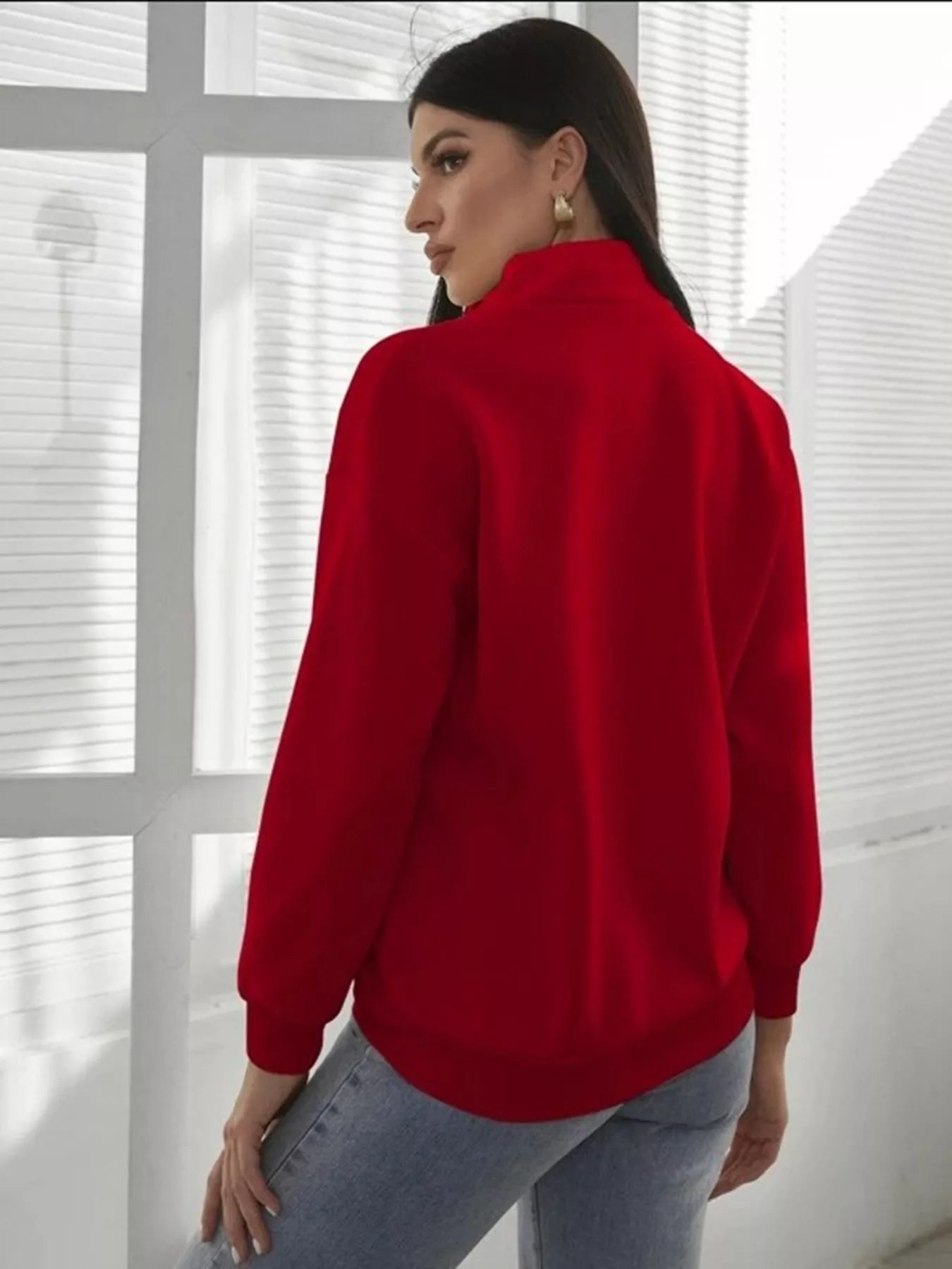 Person wearing a red sweater in front of a window with blinds