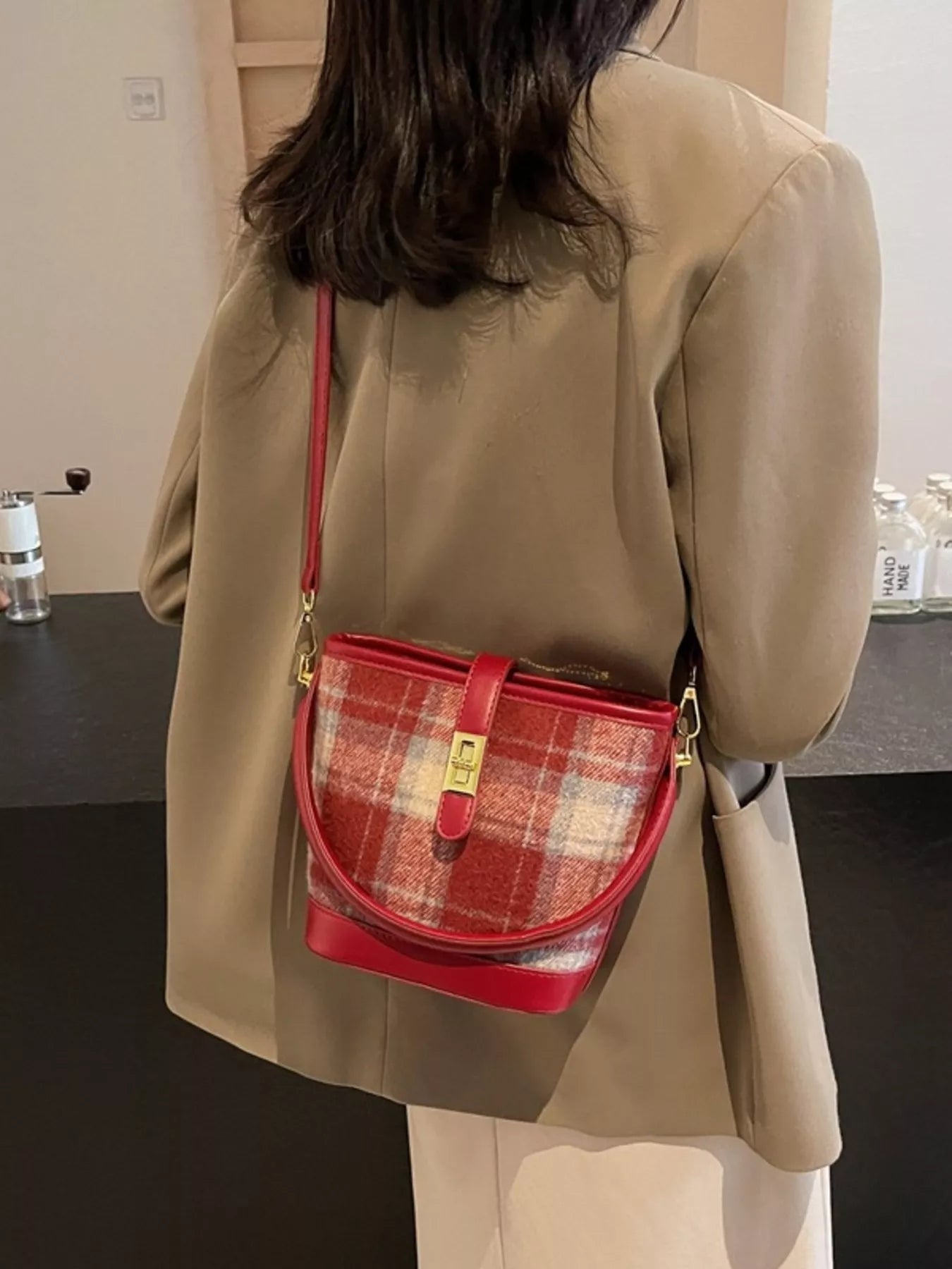 Person wearing a beige coat with a red plaid handbag over one shoulder.