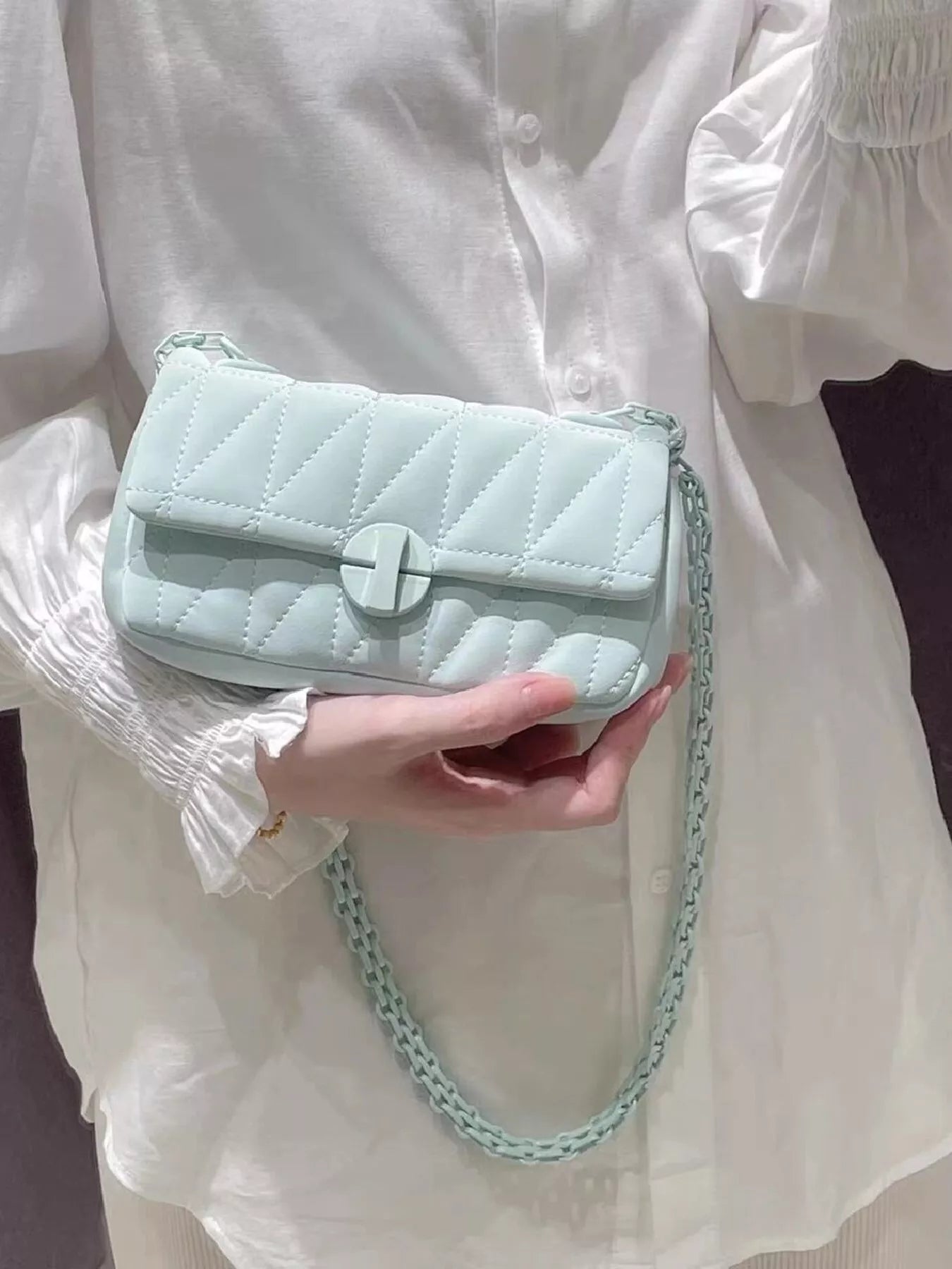Light blue quilted handbag with chain strap held by a person wearing a white blouse.