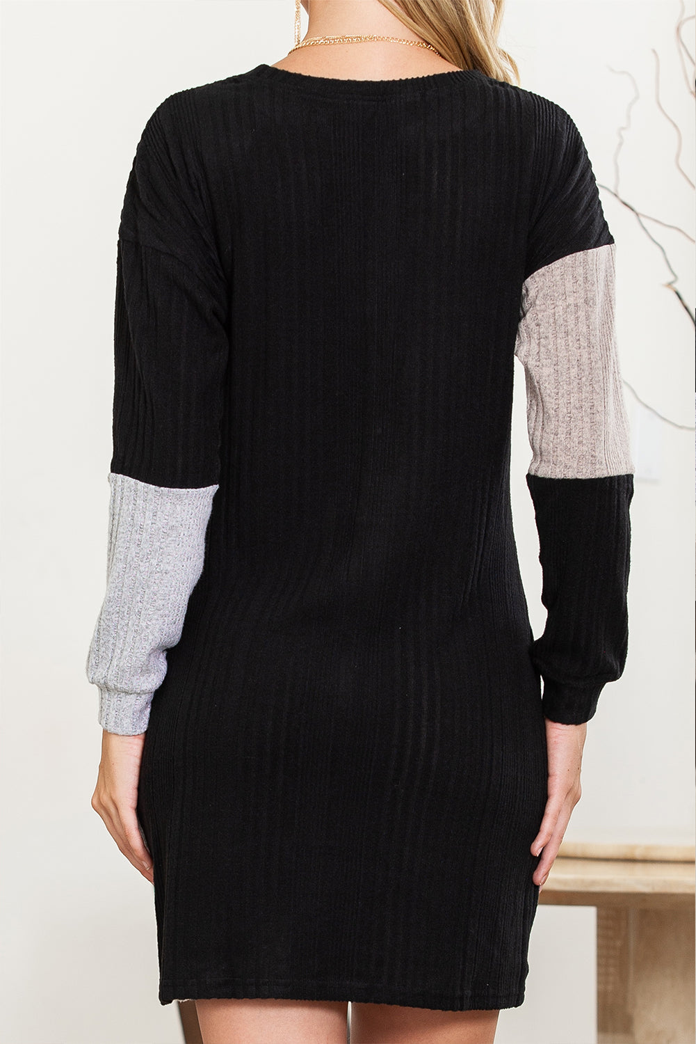 Black dress with gray sleeves worn by a person against a white background